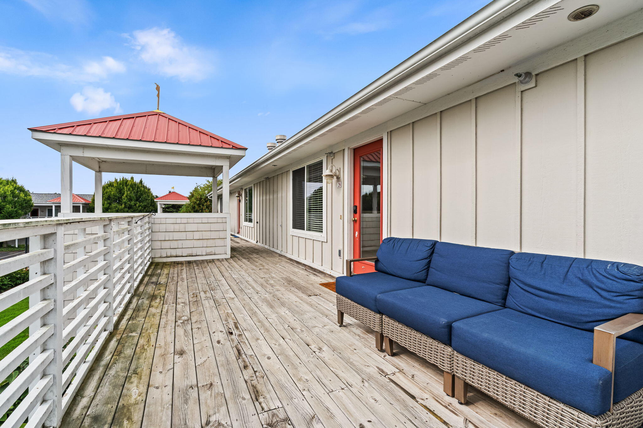 Outdoor deck with a blue-cushioned wicker sofa, white railings, and a red-roofed pavilion.