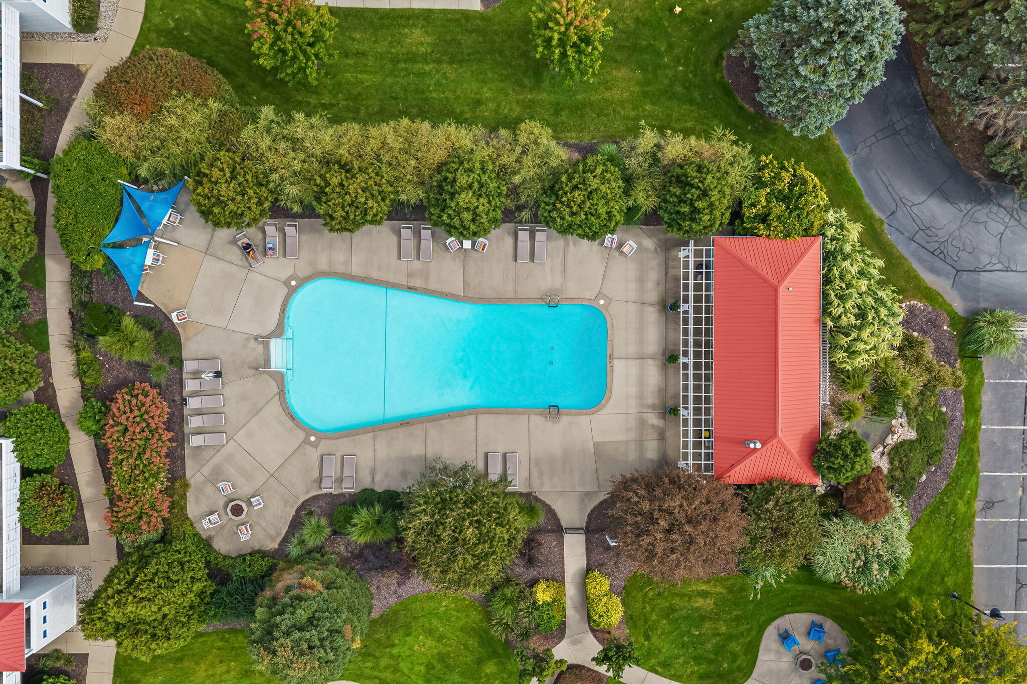 Aerial view of a swimming pool with lounge chairs, blue shade canopies, and landscaped gardens.