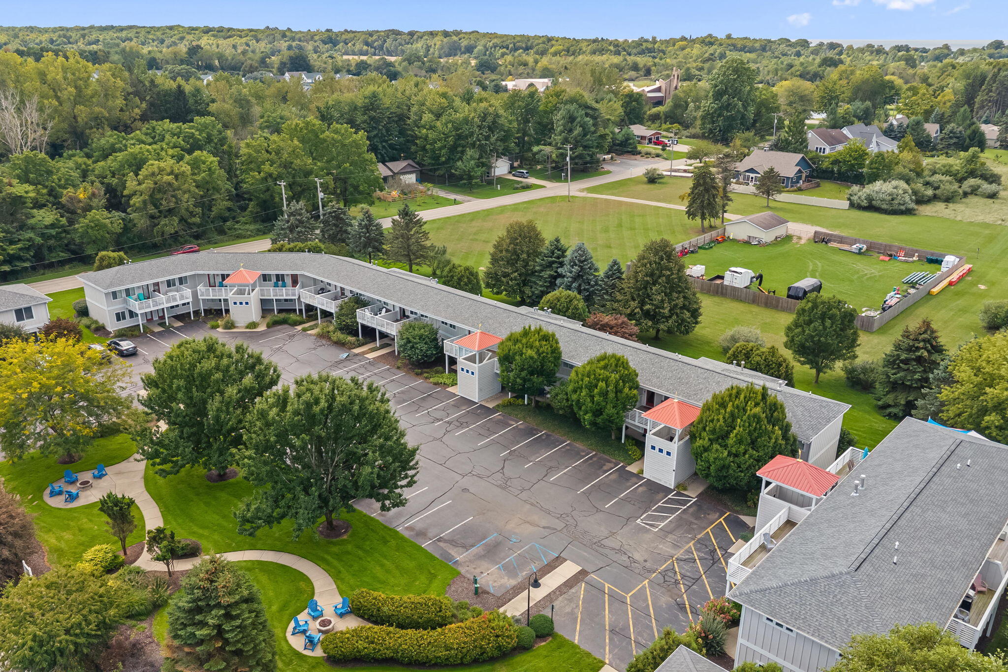 Aerial view of a multi-unit building with white balconies, red-roofed entrances, landscaped grounds and a large parking lot.