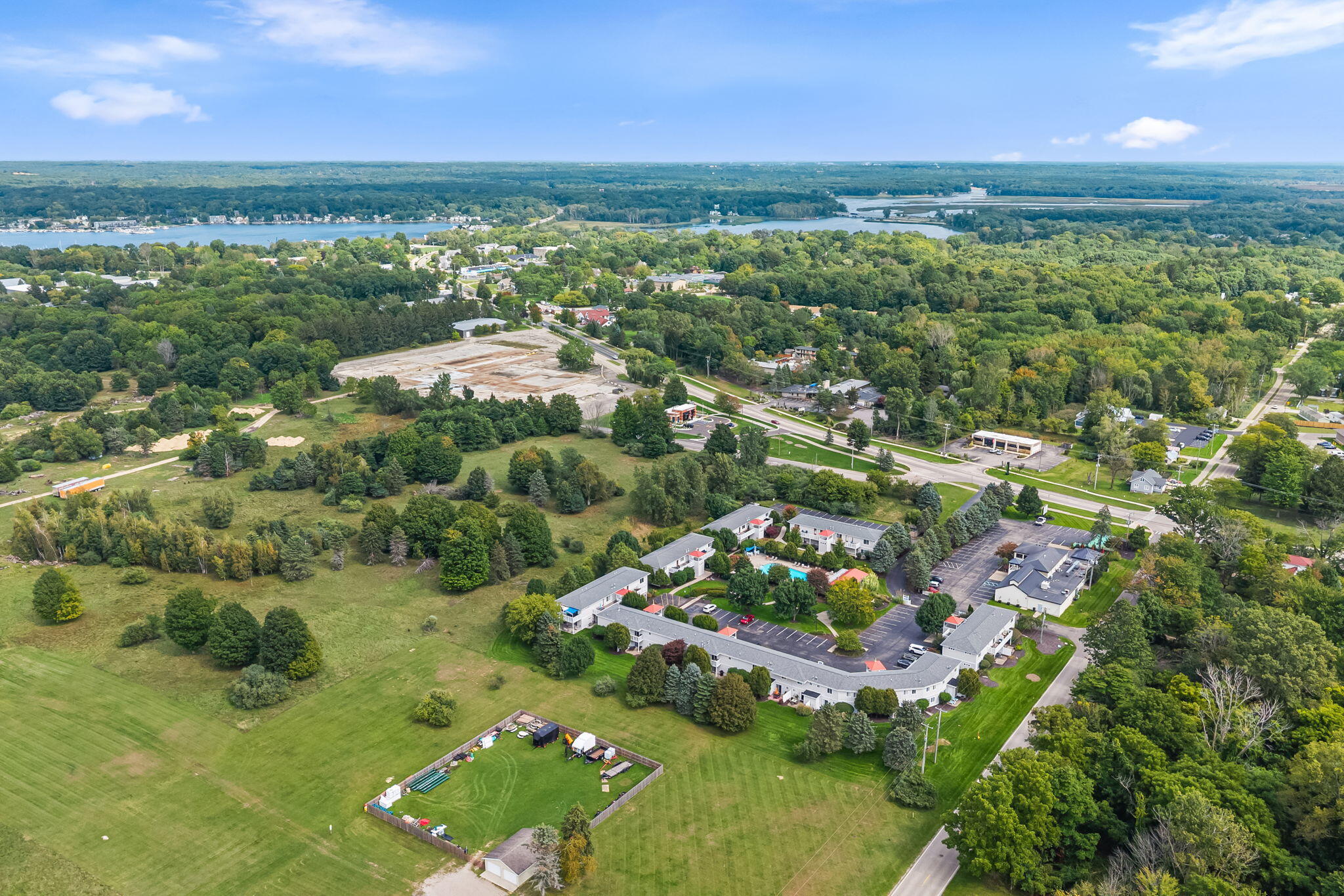 Aerial view of a residential complex with a swimming pool, broad lawns, and waterways in the distance.