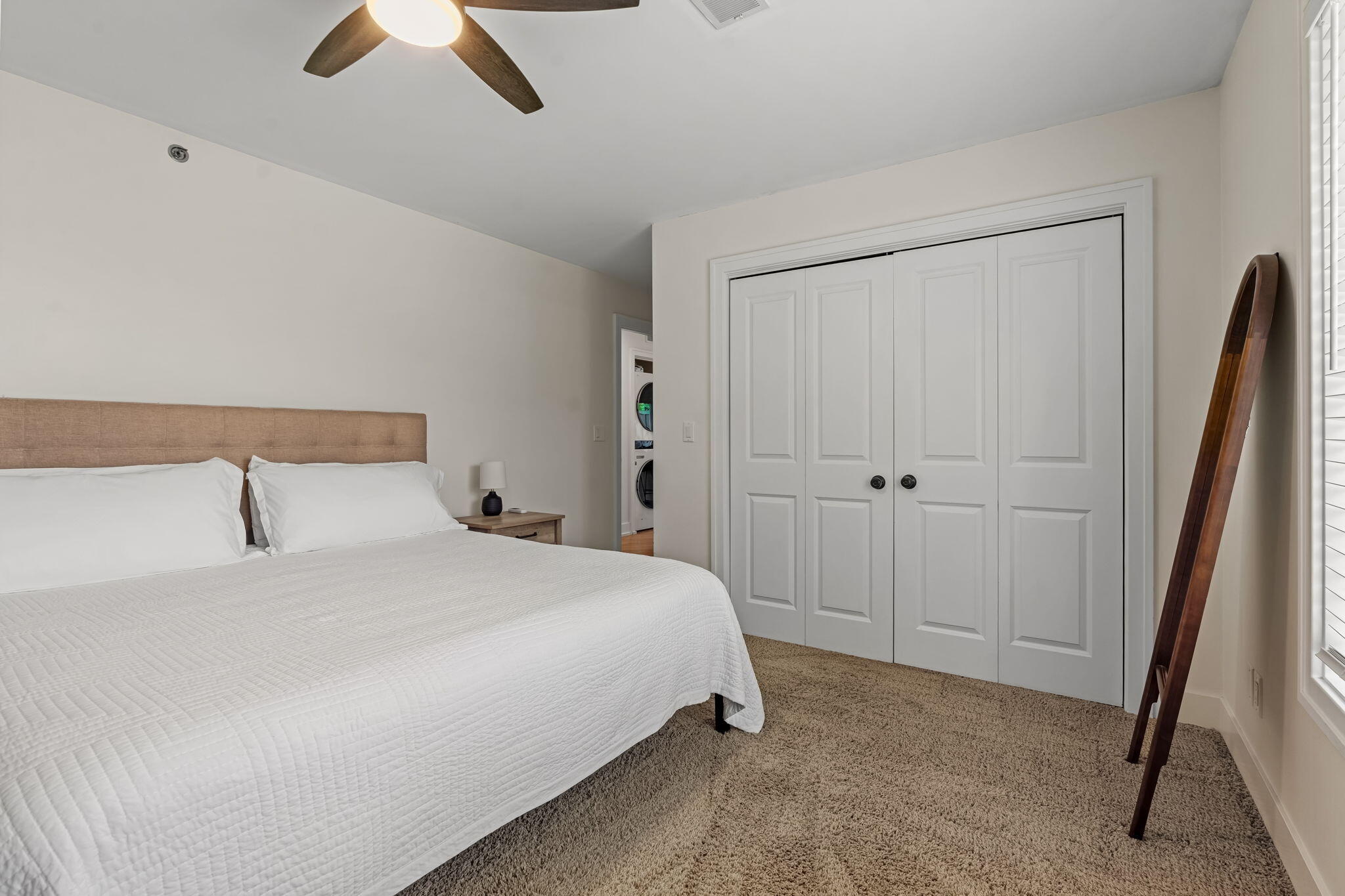 Bedroom with a large white-covered bed, double closet doors, and a washer and dryer visible through the doorway.