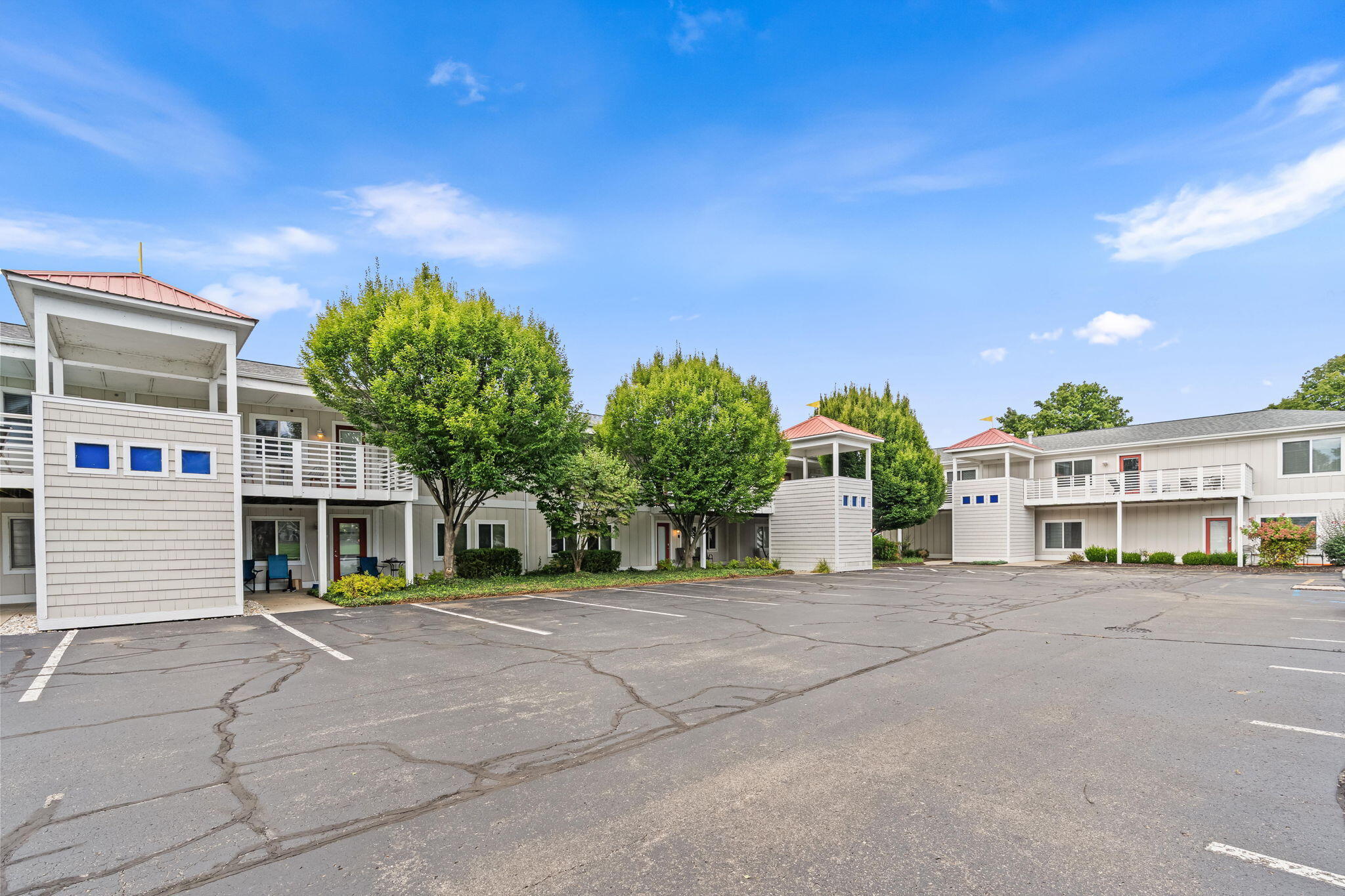 Multi-unit building with red-roofed balcony towers and a cracked asphalt parking lot.