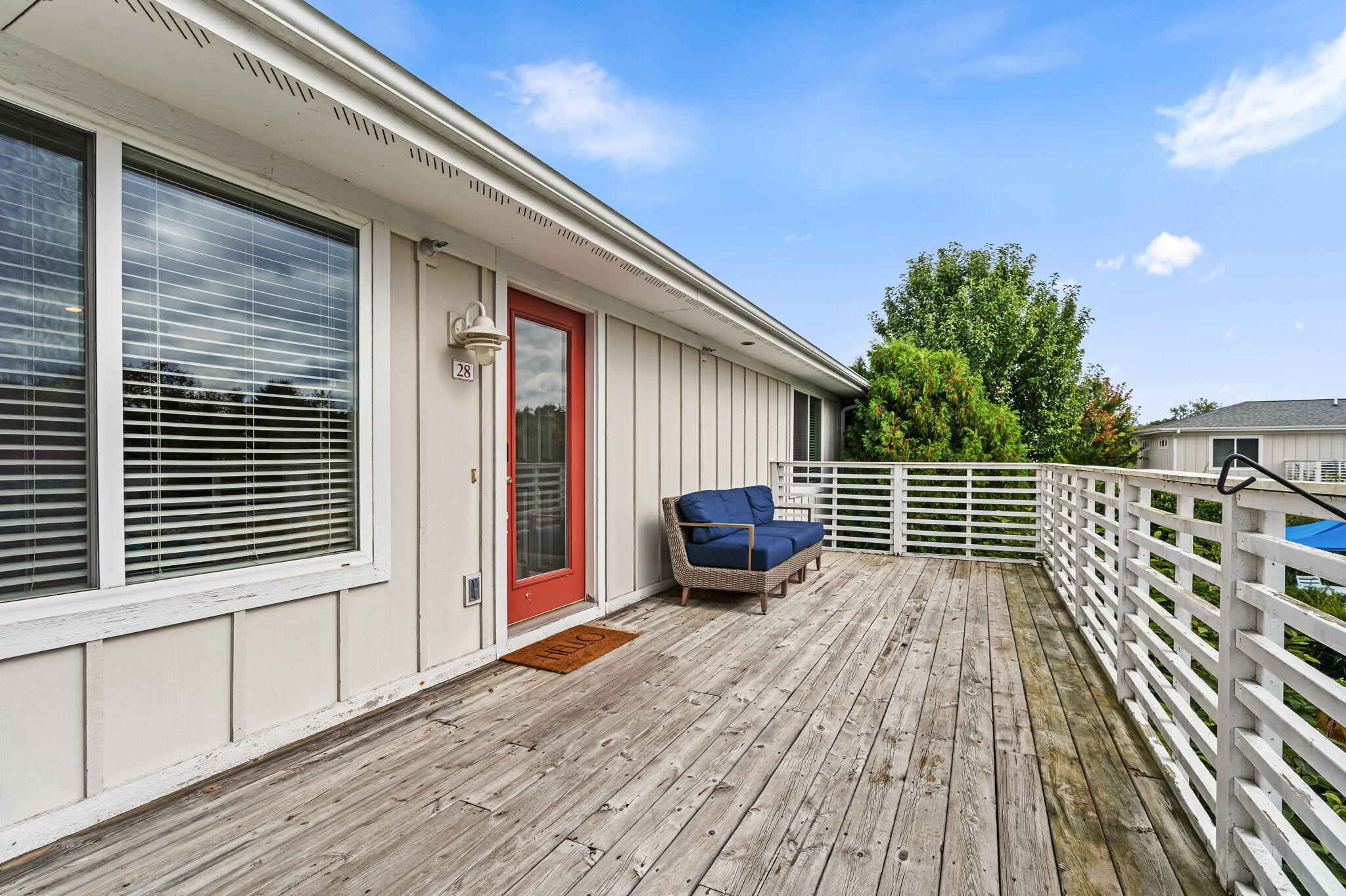 Home deck with white railings, a red-framed door marked 28, and a blue-cushioned loveseat.
