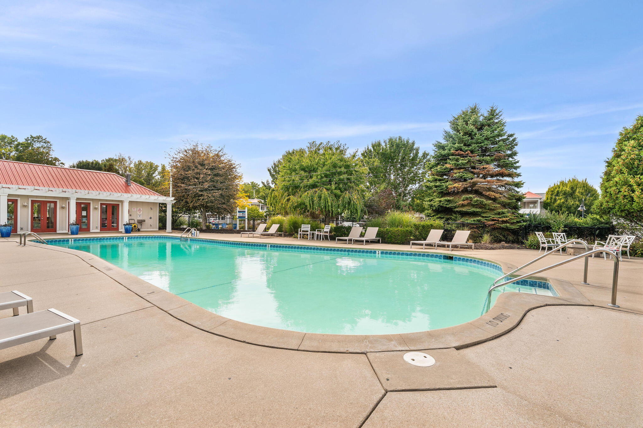 Outdoor swimming pool with turquoise water, lounge chairs, and landscaped trees.
