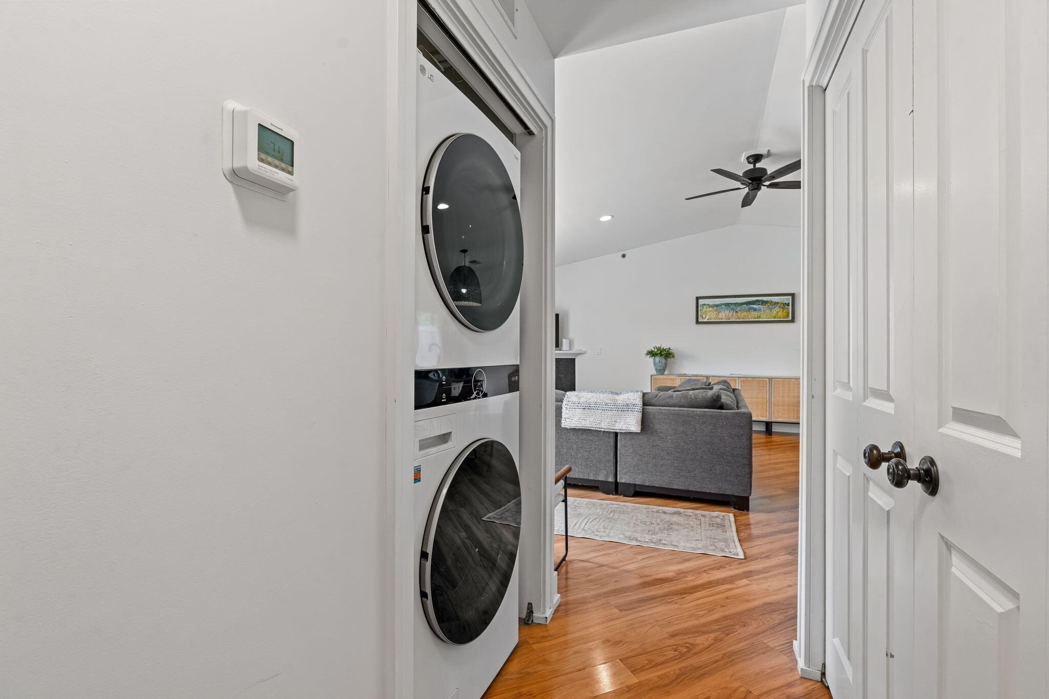 Stacked washer and dryer beside a doorway opening onto a living room with hardwood floors.