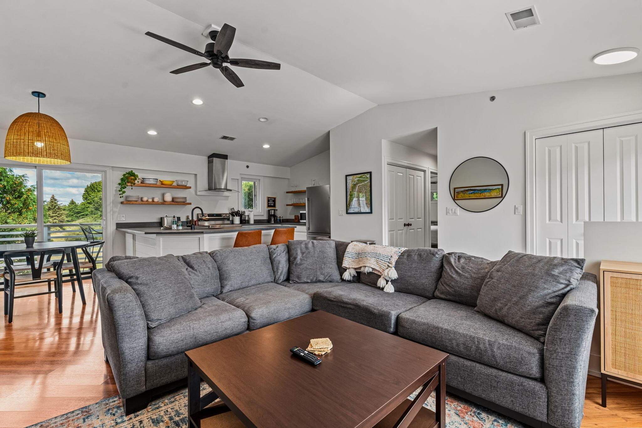 Open-plan living room with a large gray sectional facing the kitchen and balcony doors.