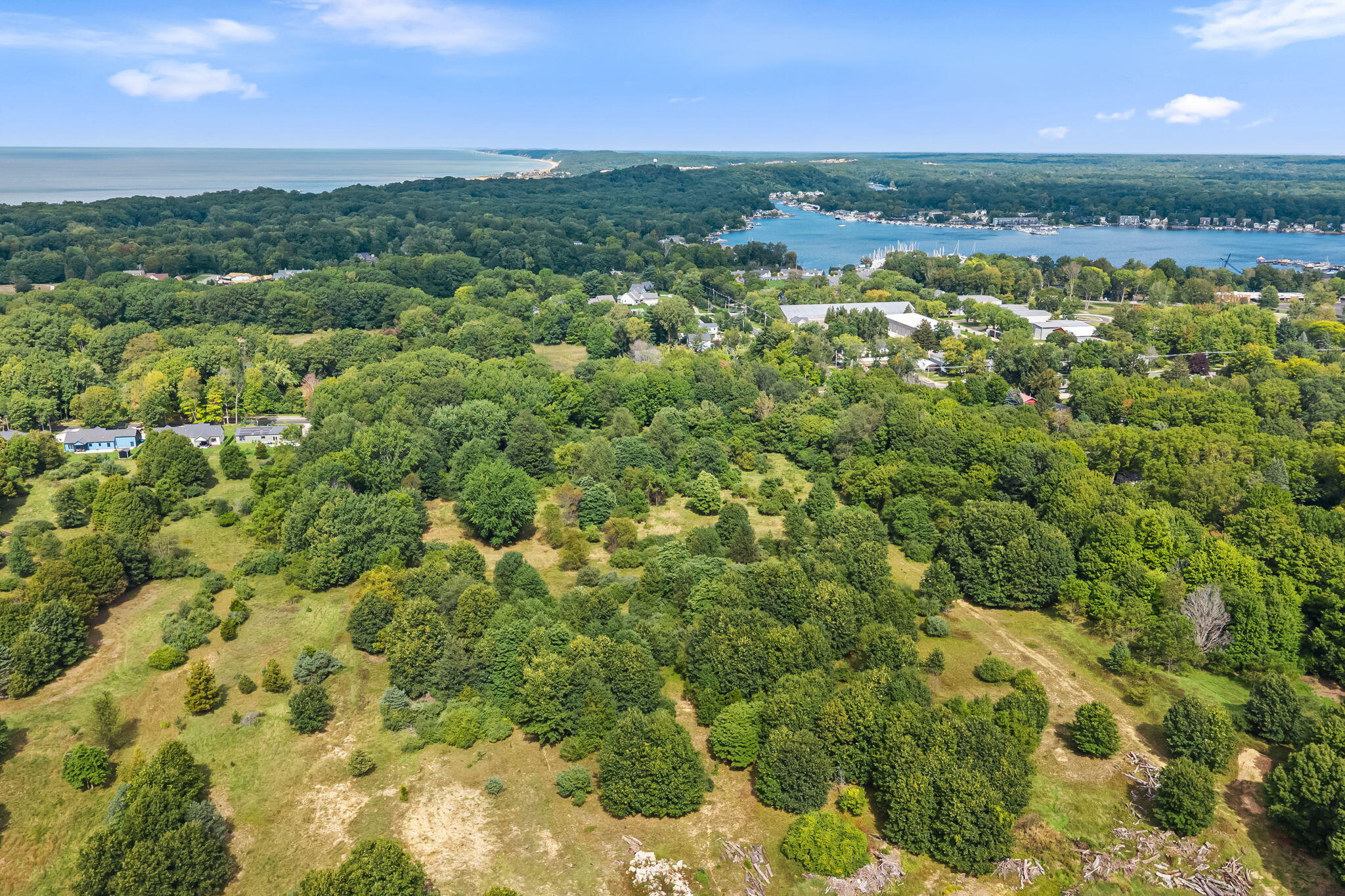 Aerial view over wooded land toward a harbor and distant shoreline.