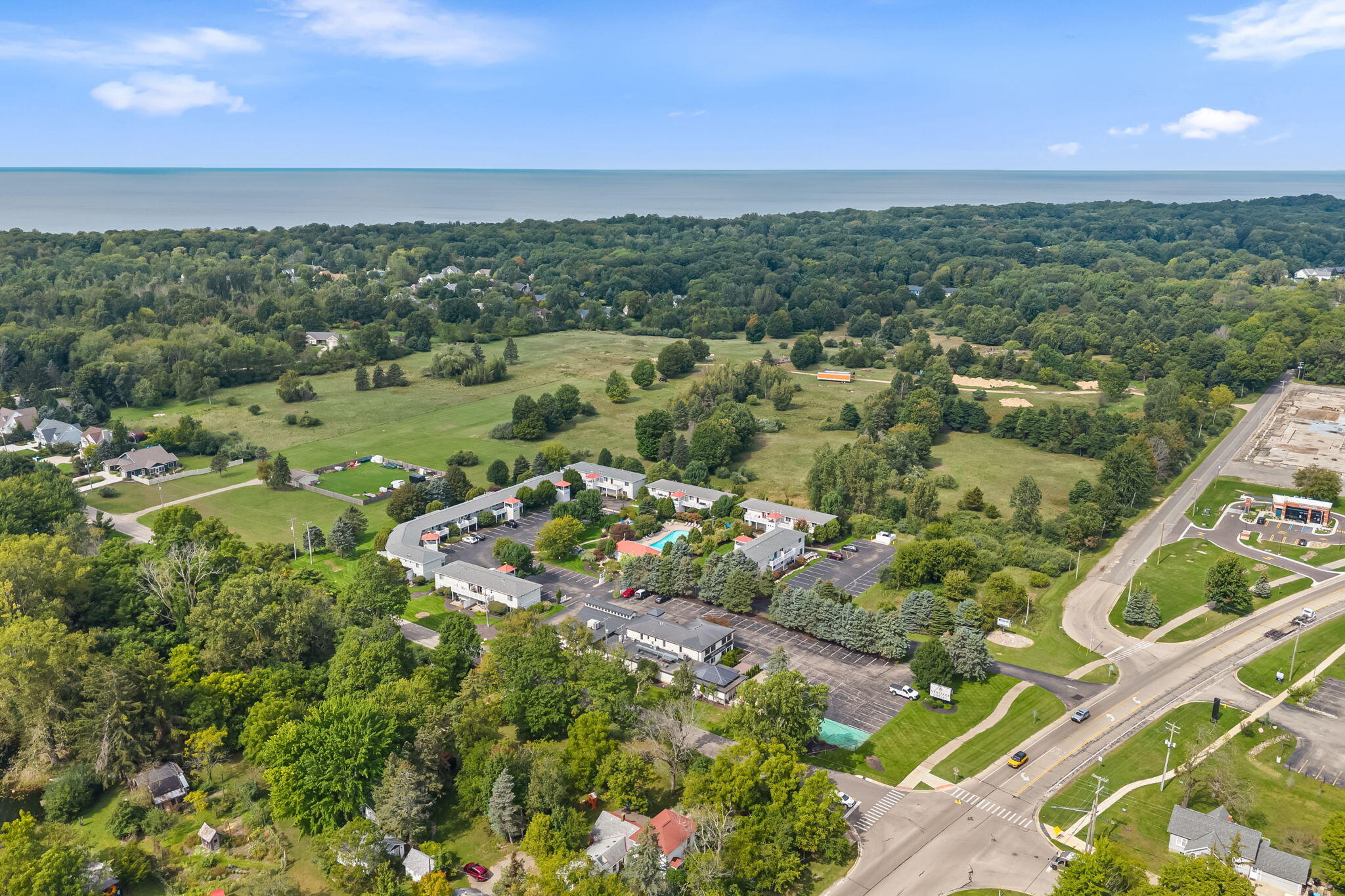 Aerial view of a tree-surrounded property complex with a pool and water on the horizon.