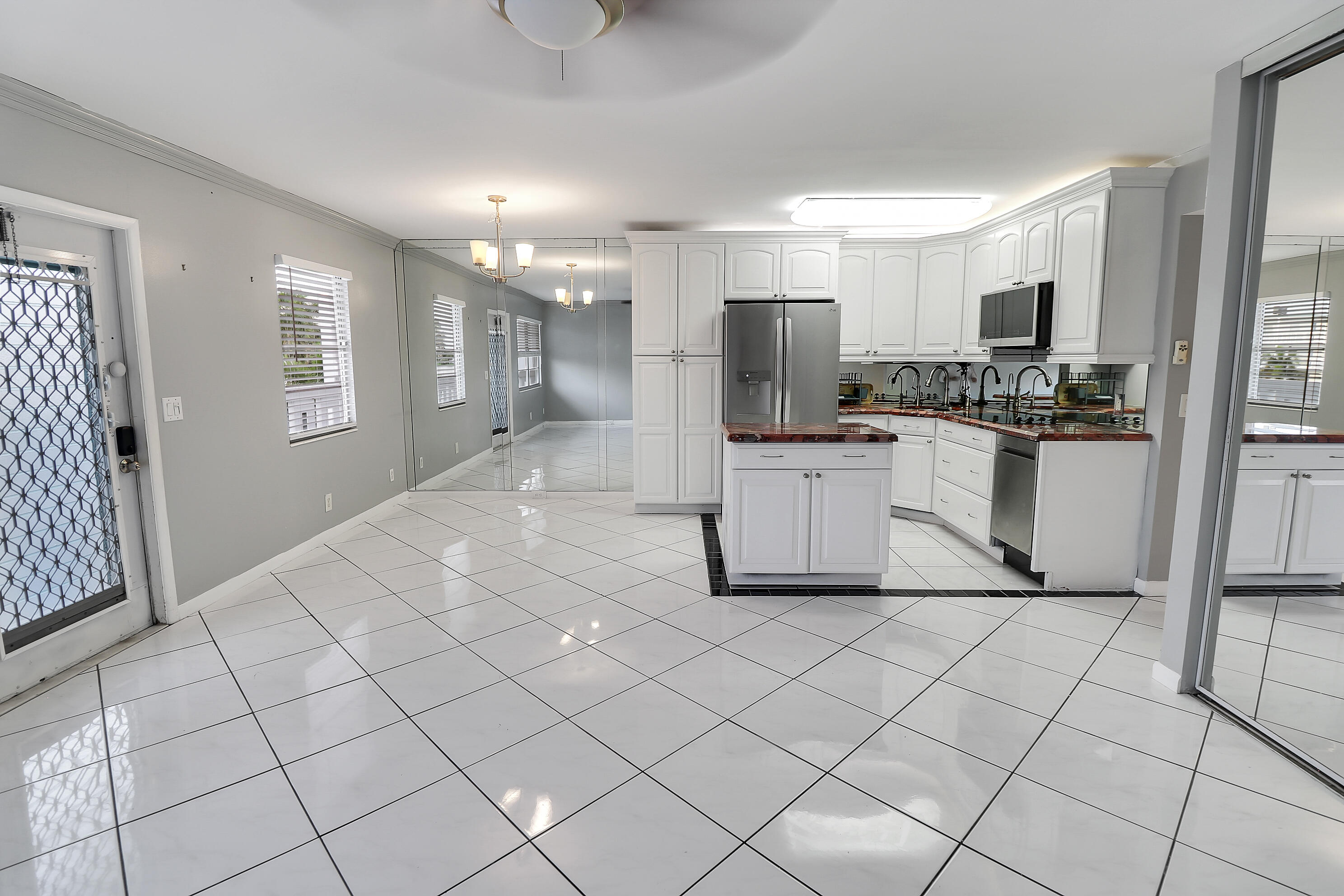 Kitchen with white cabinetry, stainless appliances, mirrored walls, and glossy white tile floors.