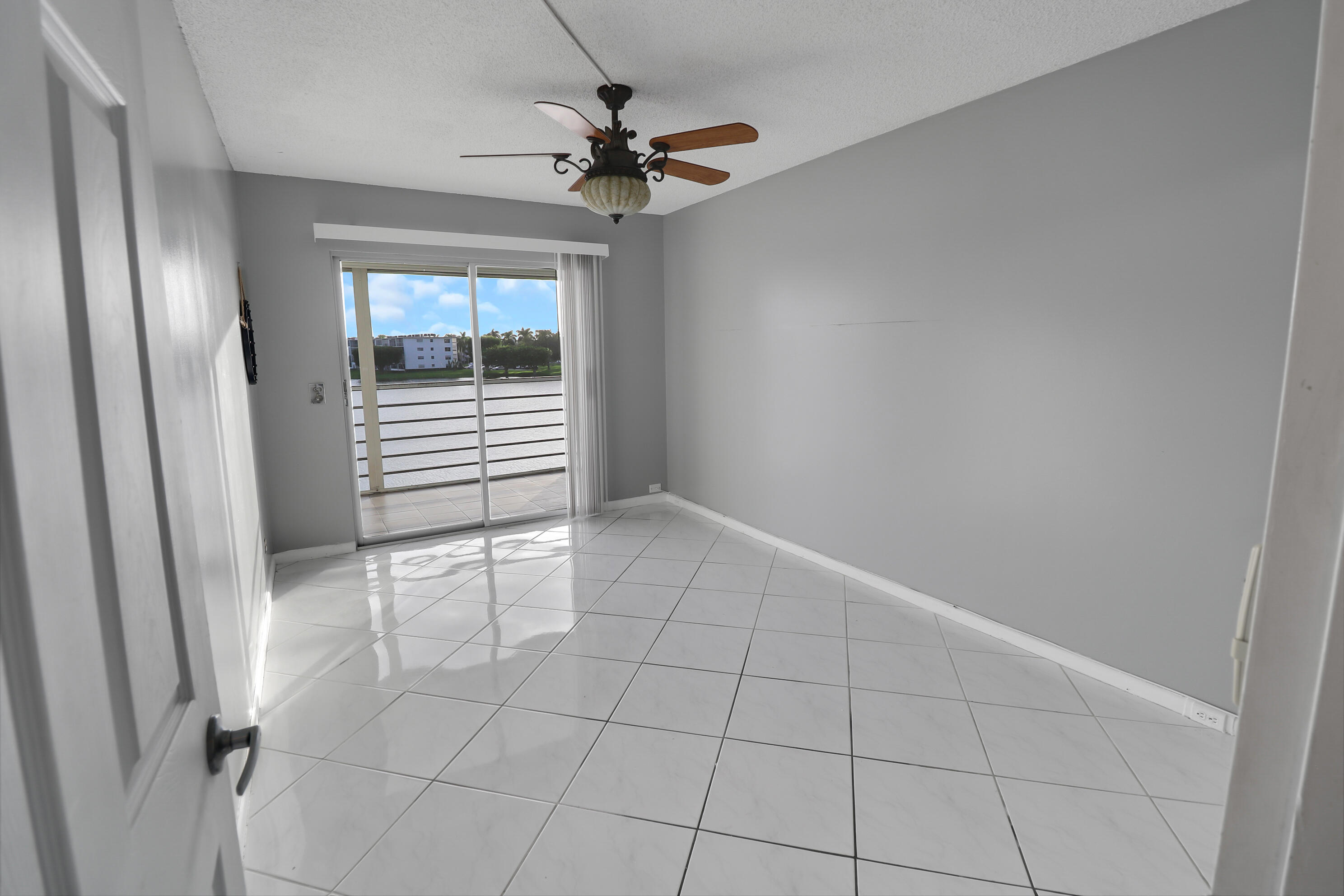 Empty tiled room with a ceiling fan and sliding glass doors opening to a balcony.
