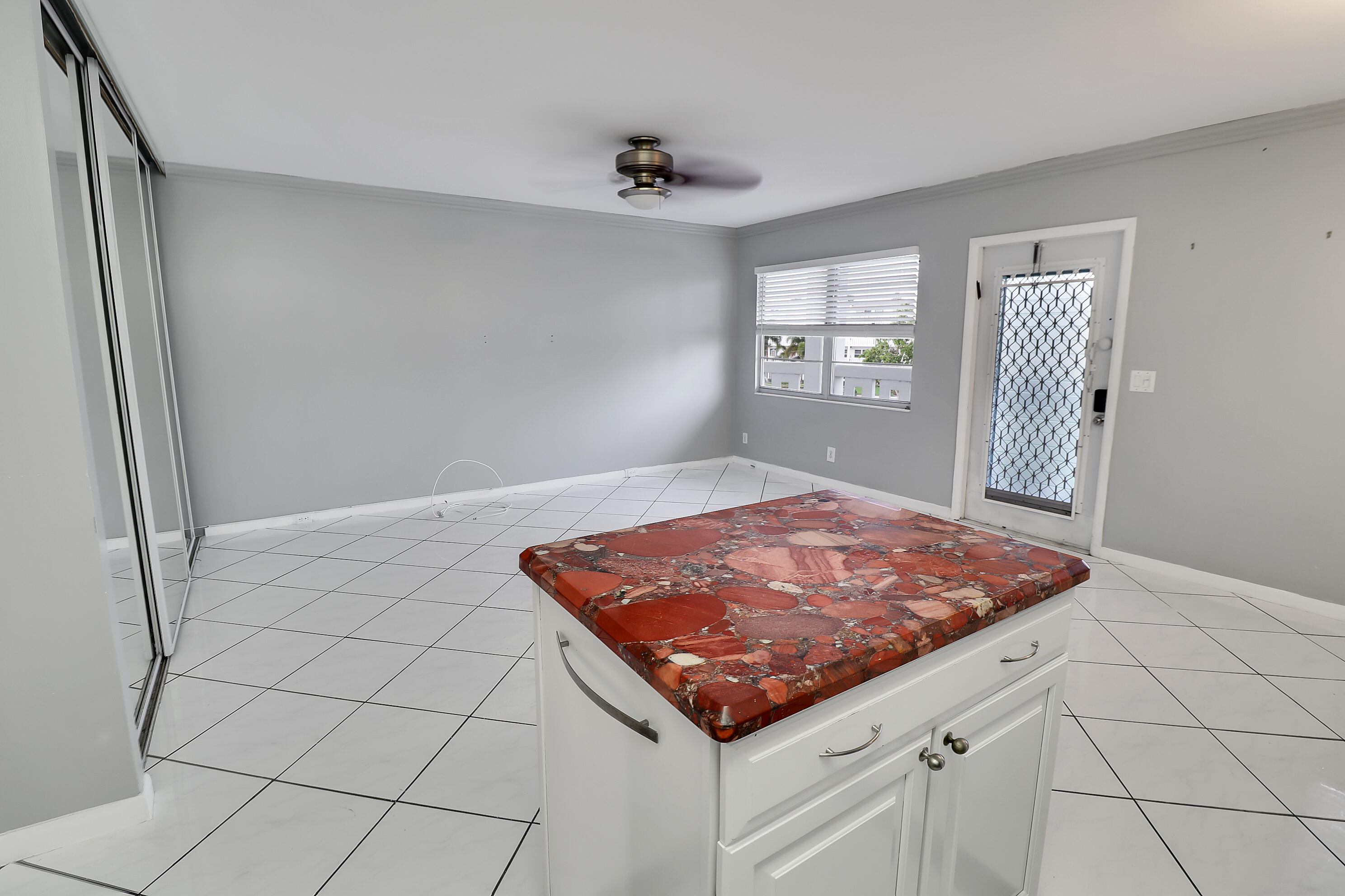 Empty tiled room with a white island topped by distinctive red patterned stone.