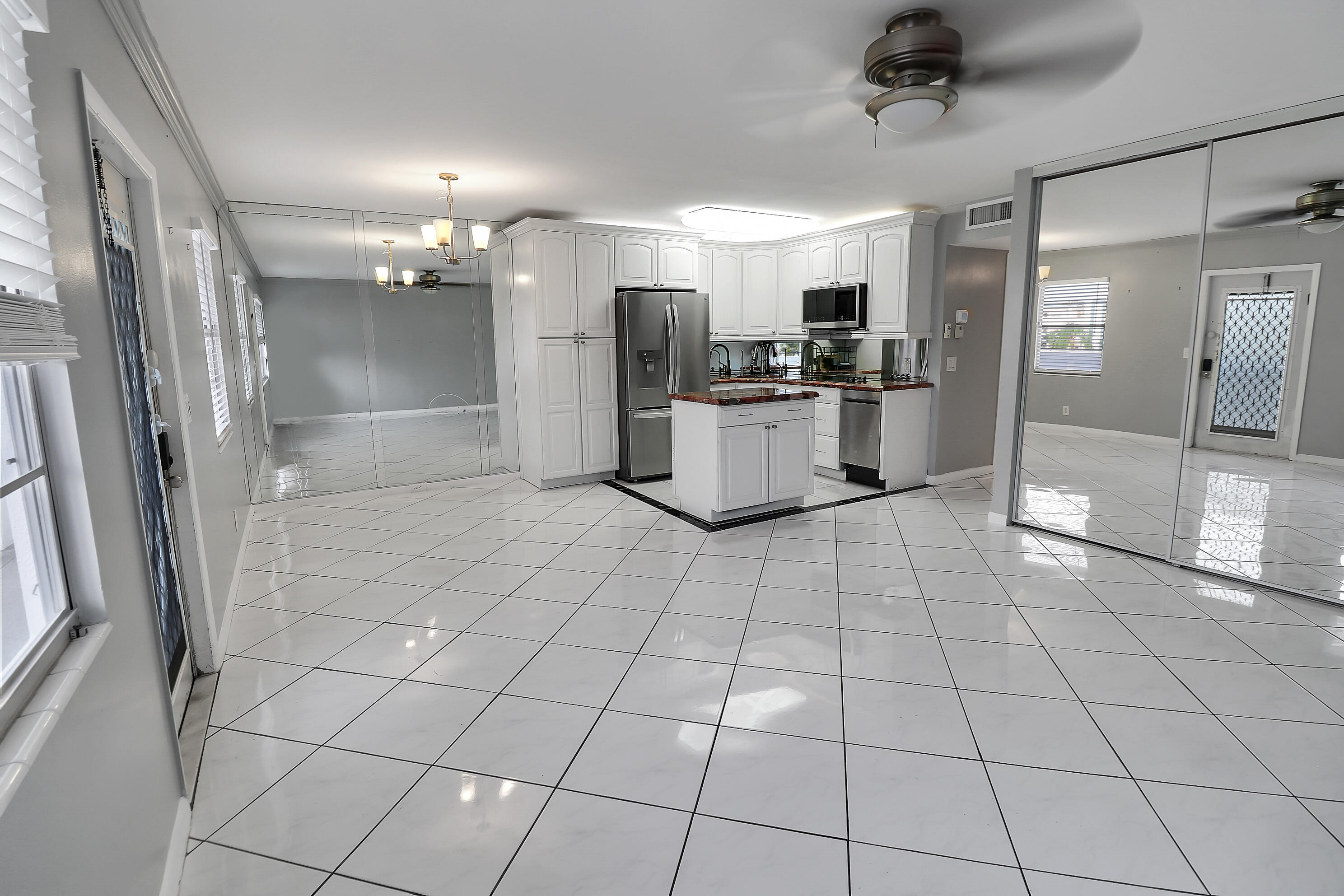 Open kitchen with white cabinetry, a central island, stainless appliances, and glossy tile floors.