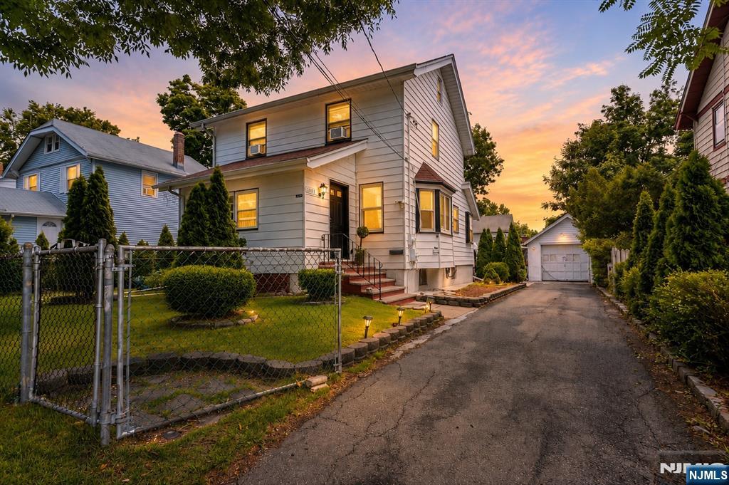 Two-story house with a fenced yard and detached garage, photographed at sunset.
