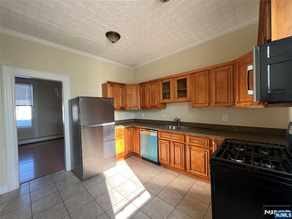 Kitchen with warm wood cabinets, stainless-steel appliances, and sunlight across the tiled floor.
