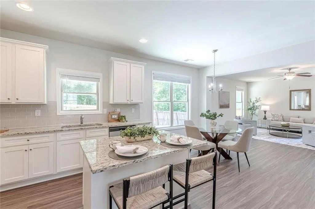 Open kitchen with a granite island and breakfast stools adjoining a staged dining and living area.