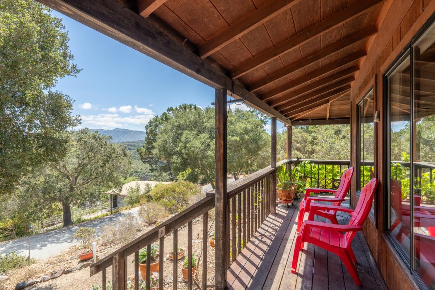 Covered wooden deck with red chairs overlooking wooded hills.