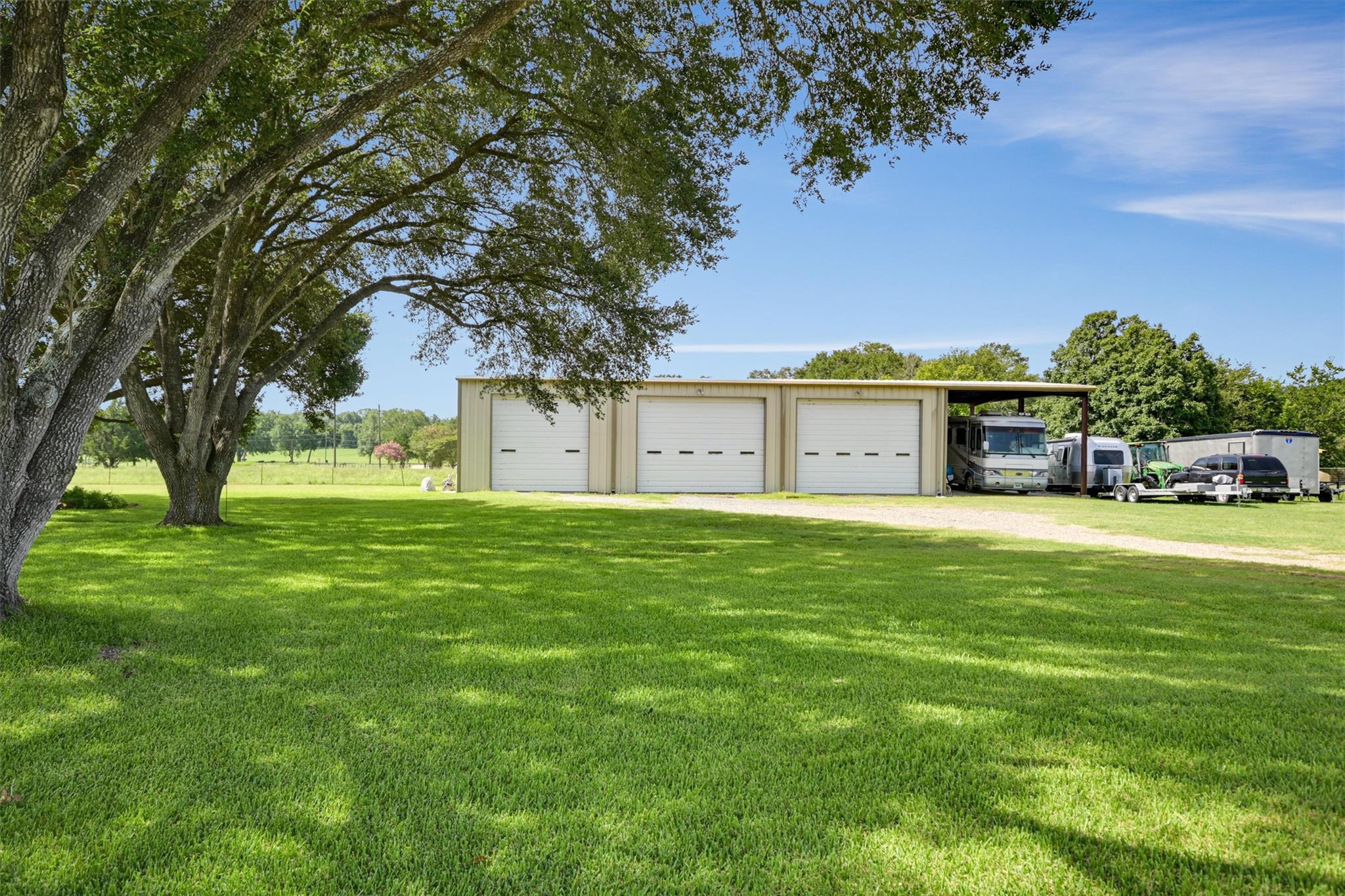 Three-bay garage with covered RV parking, parked vehicles, and a large shaded lawn.
