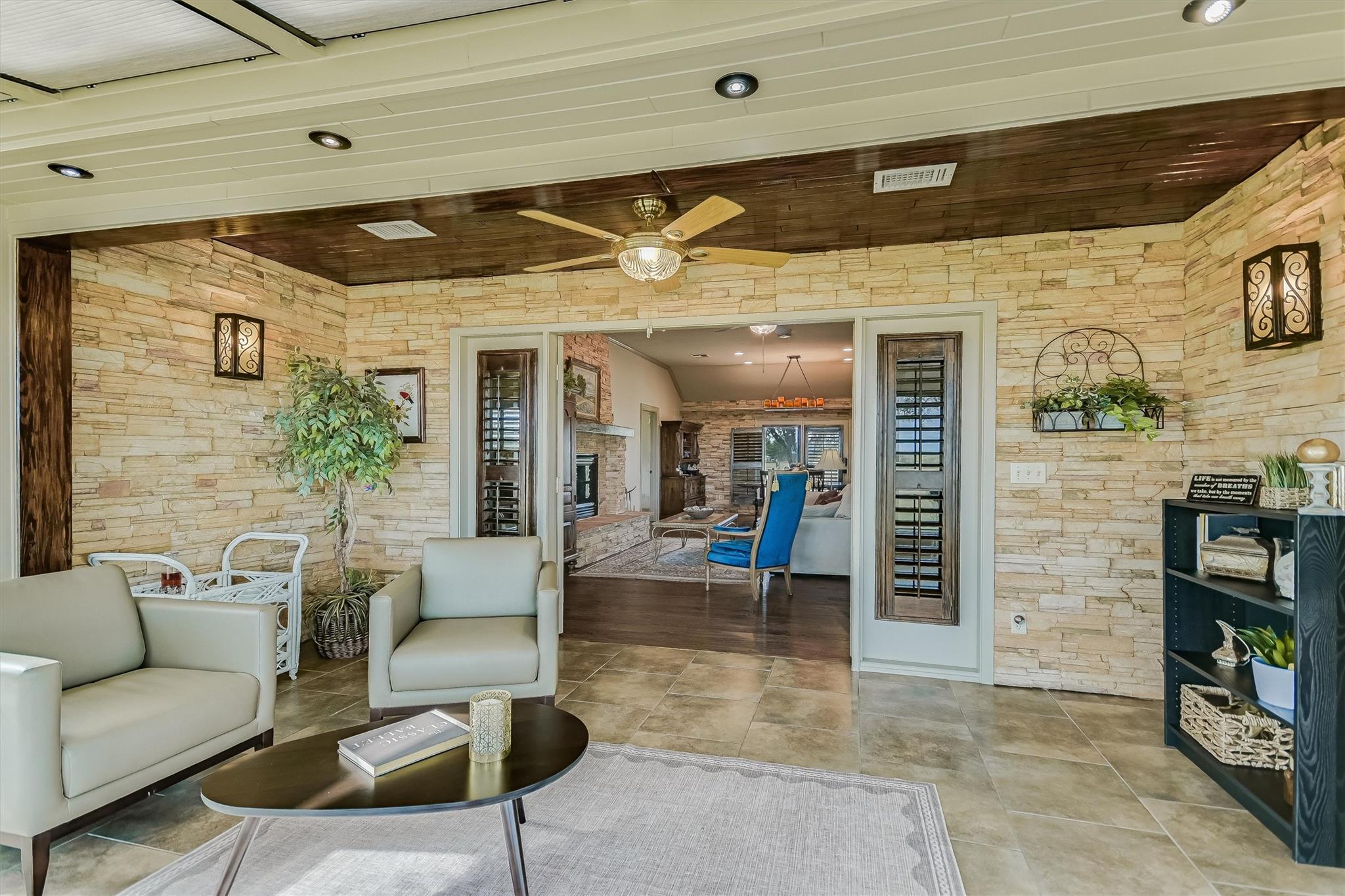 Stone-walled sitting area with tiled floors and a wide opening to a living room with a fireplace.
