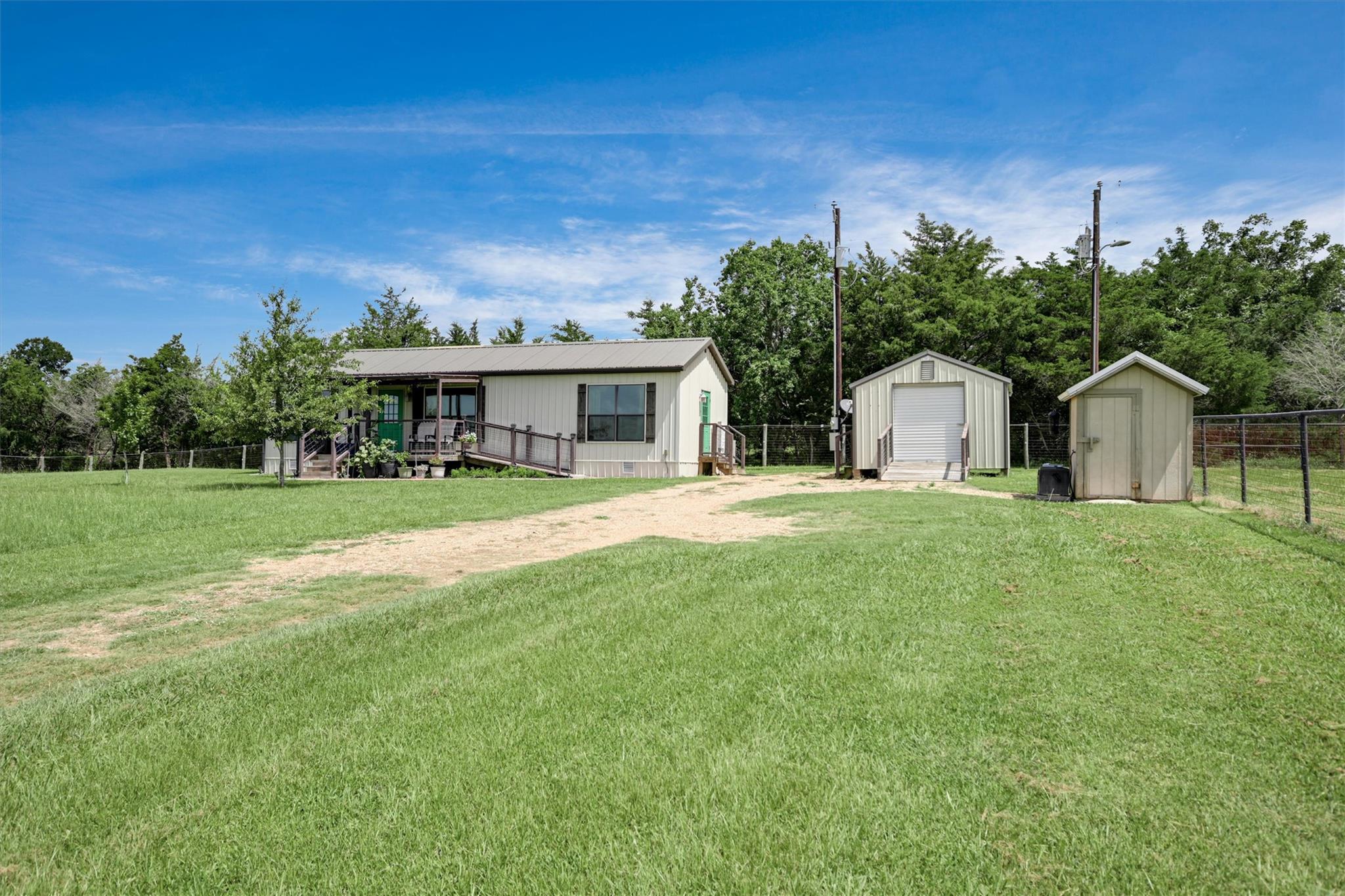 Manufactured home with covered porch, grassy yard, gravel drive, and two outbuildings.