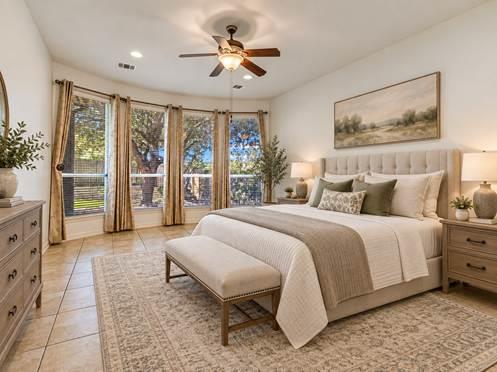 Staged bedroom with a king bed, upholstered headboard, ceiling fan, and tall patio windows.