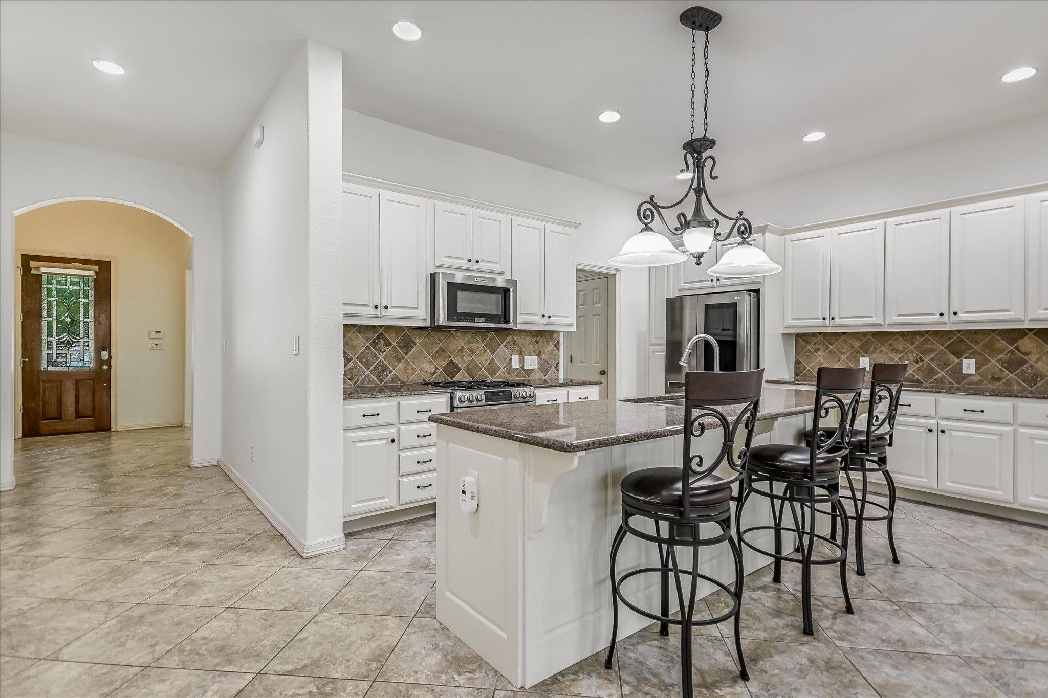 Kitchen with a large granite island, white cabinets, stainless steel appliances, and dark bar stools.