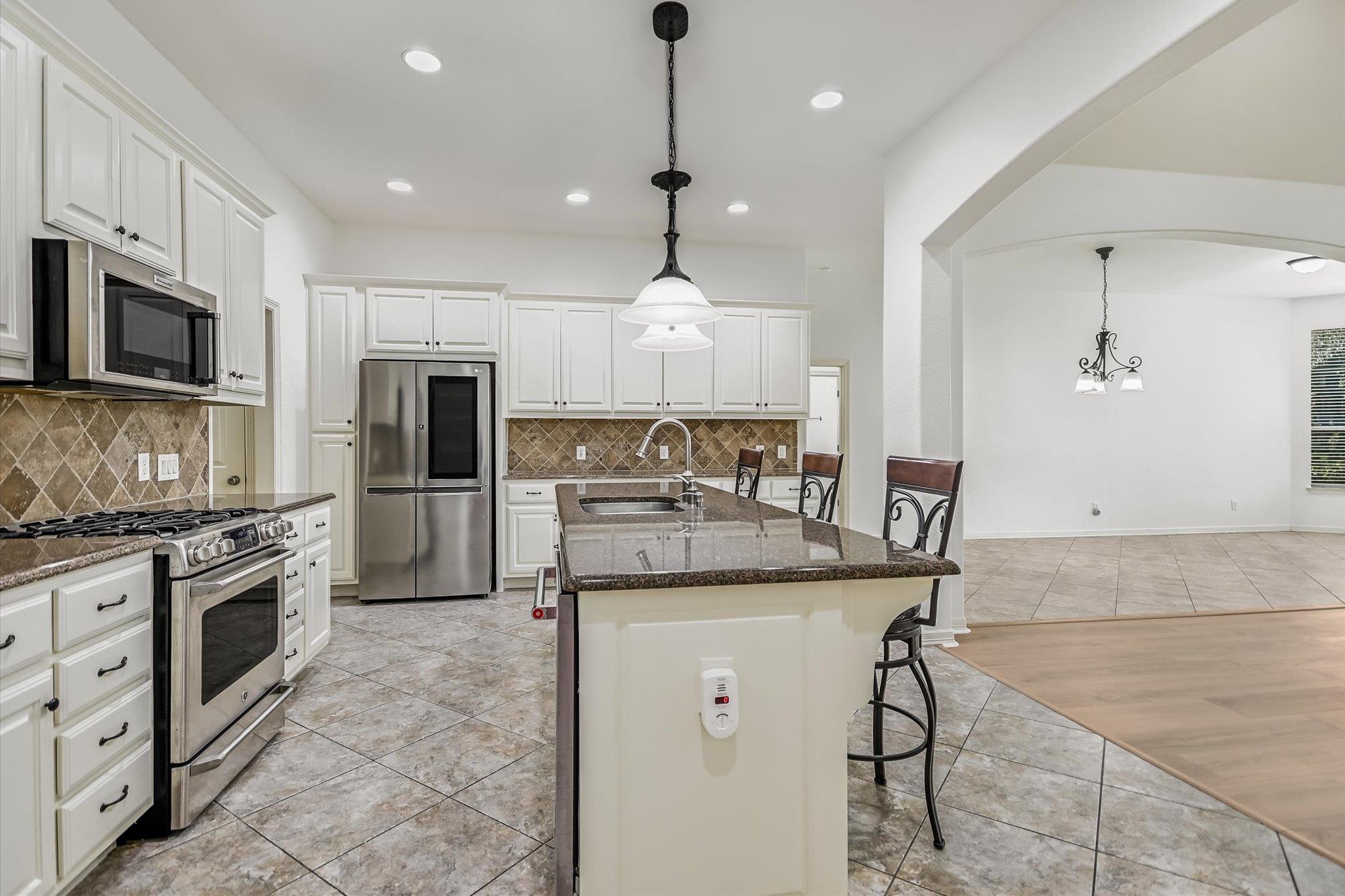 Kitchen with white cabinets, stainless steel appliances, and a large island opening onto a dining area.