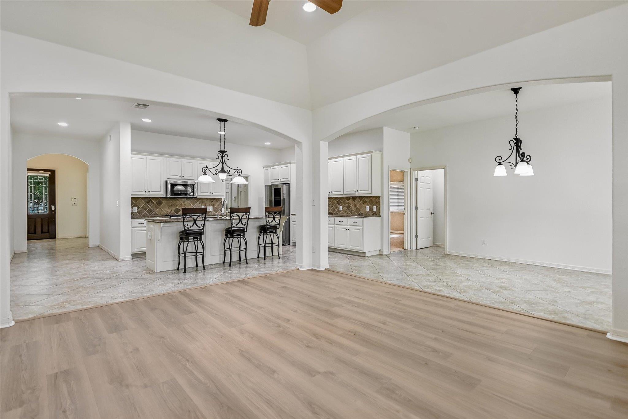 Open-plan living area with light wood flooring, arched openings, and a white kitchen with island seating.