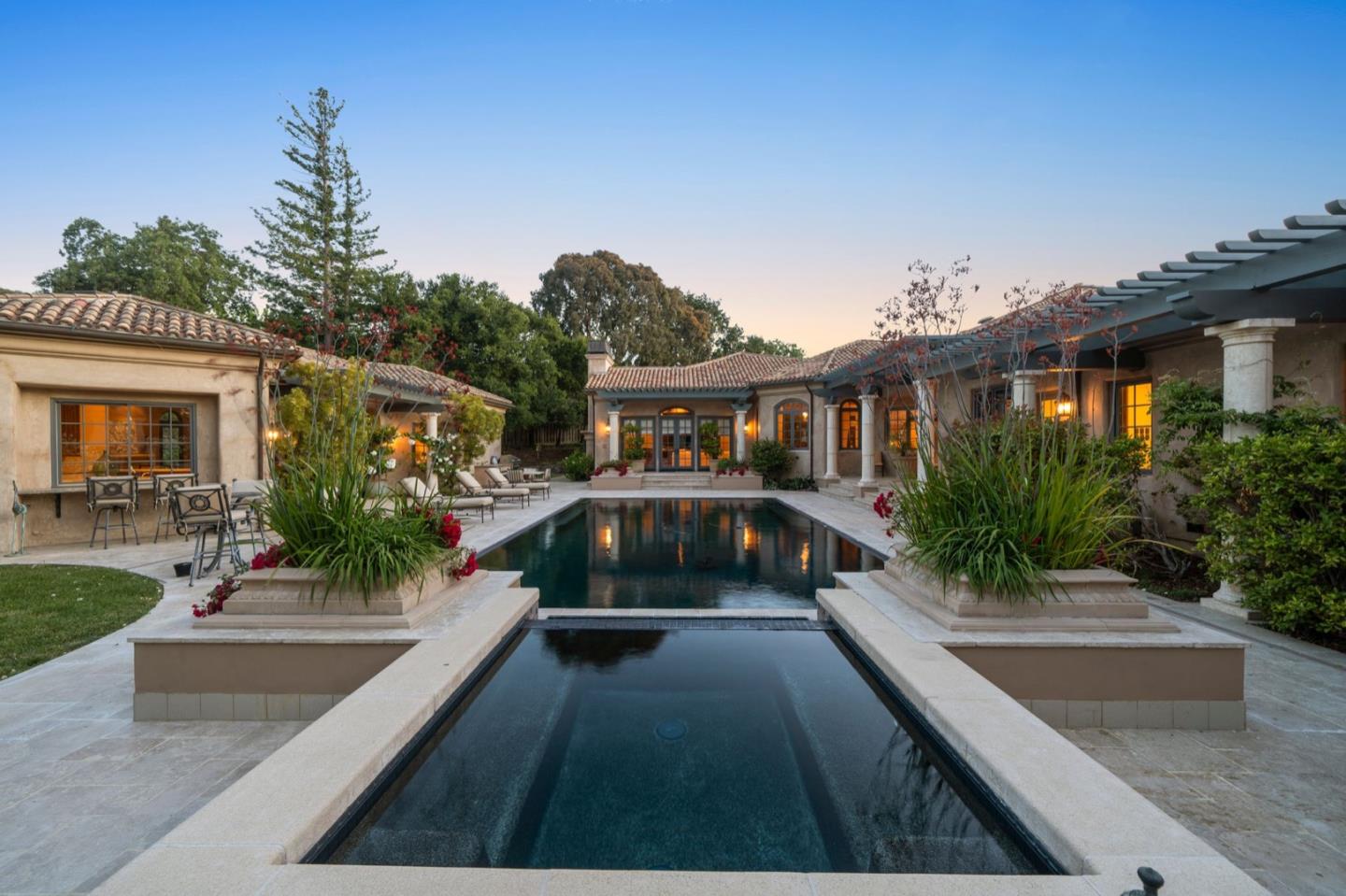 Mediterranean-style home courtyard with a long reflecting pool and warmly lit windows at dusk.