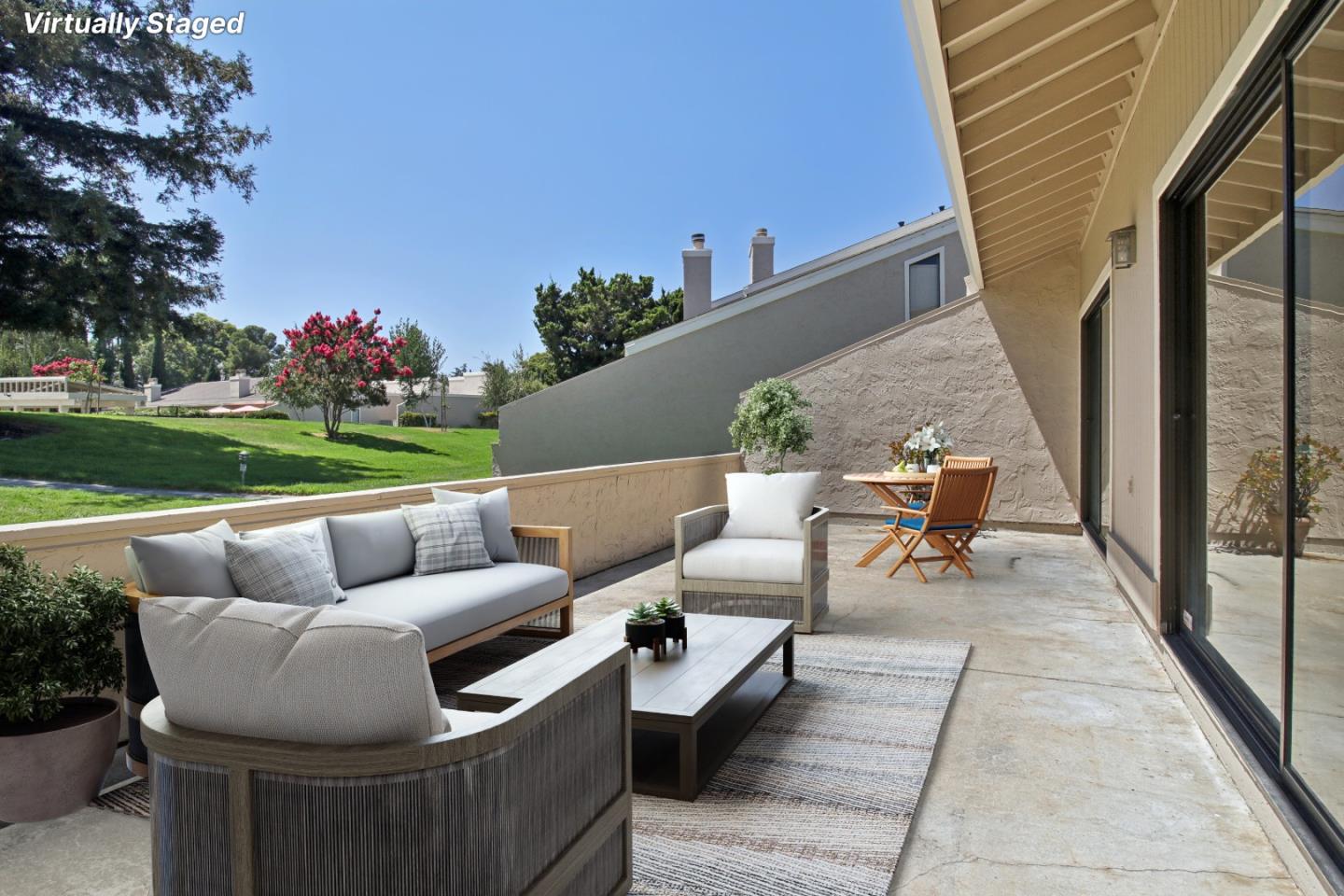 Virtually staged patio with outdoor seating and dining furniture overlooking a green lawn and flowering trees.