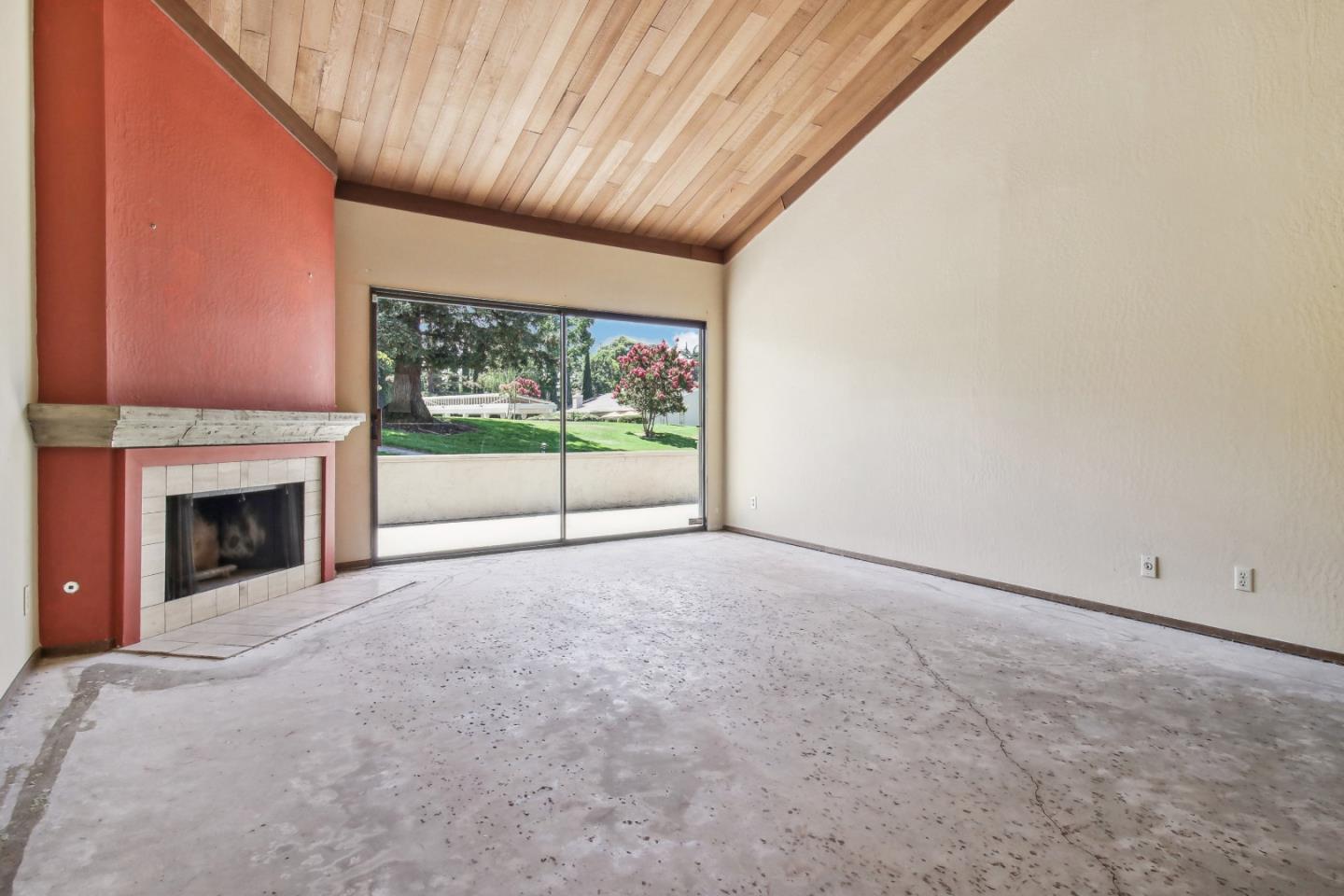 Vacant living room with a red fireplace and vaulted wood ceiling opening onto a lawn.