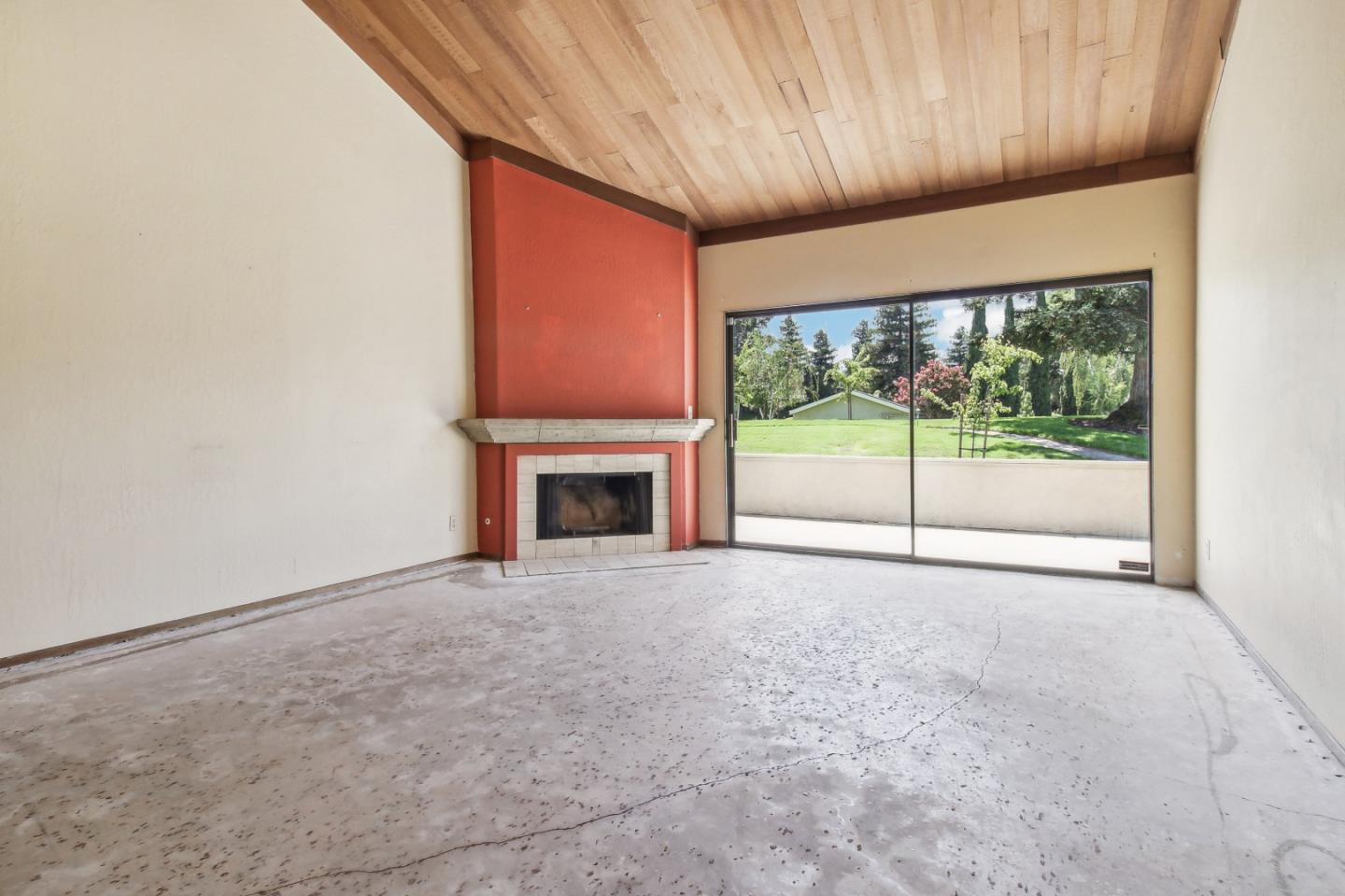 Vacant living room with a fireplace, vaulted wood ceiling, and sliding glass doors facing a lawn.