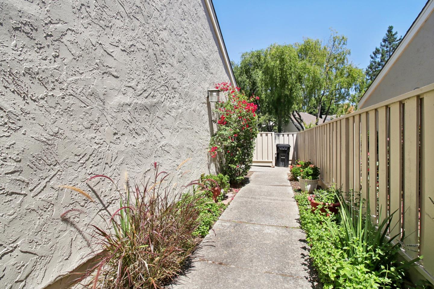 Concrete walkway beside a stucco home, bordered by flowers and a wooden railing.