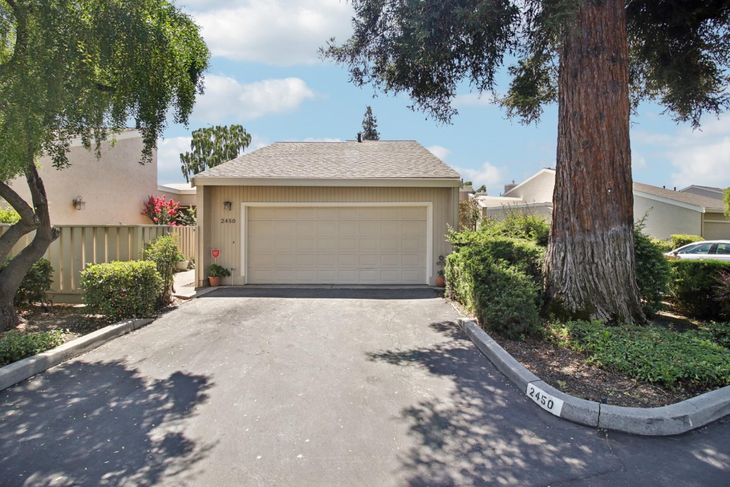Home exterior with a two-car garage, wide driveway, and large shade tree.