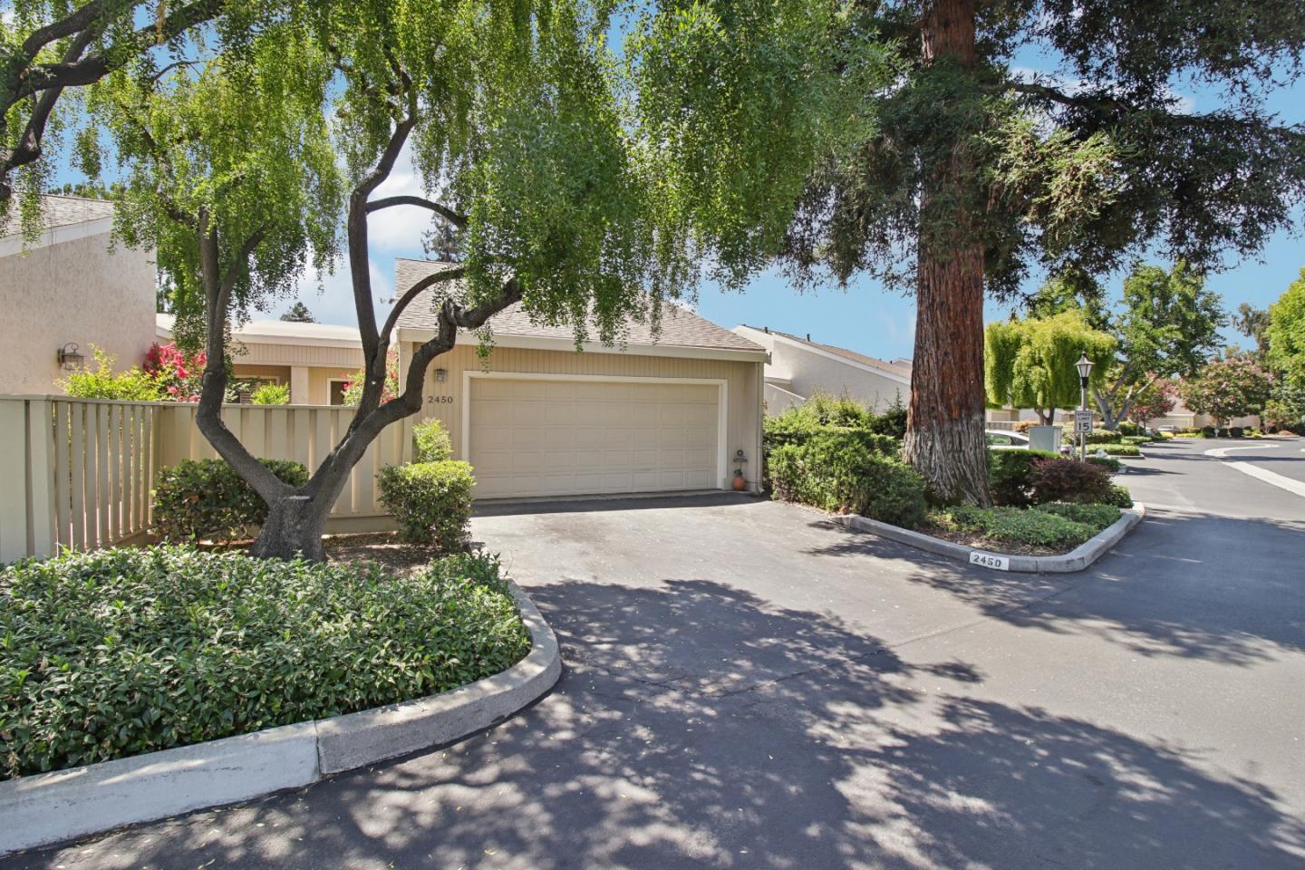 Home with an attached double garage, shaded by mature trees and surrounded by landscaped shrubs.