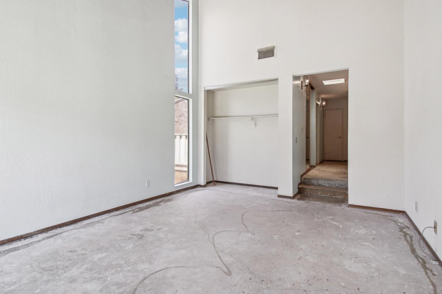 Empty interior room with tall narrow windows, a closet alcove, and a worn concrete floor.