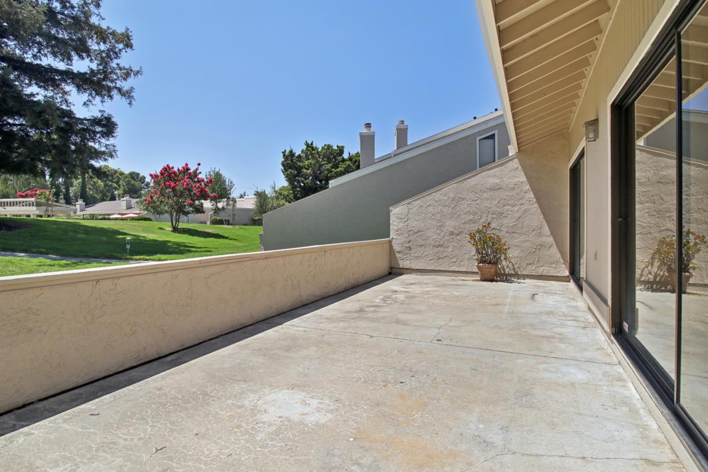 Concrete patio beside sliding glass doors, overlooking a green lawn and flowering tree.