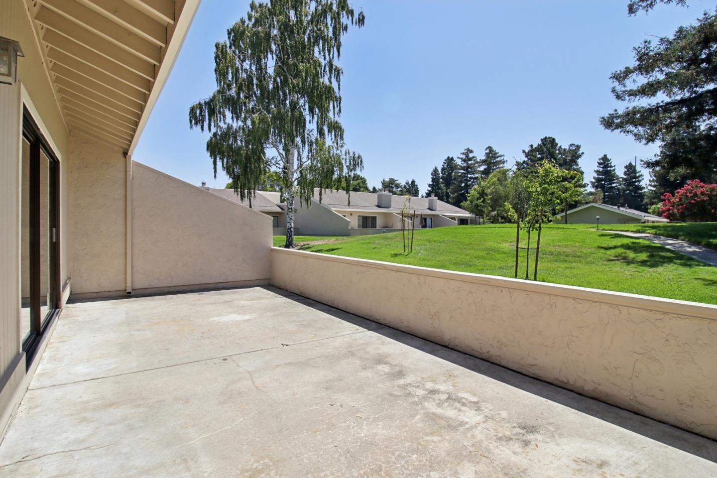 Concrete patio with low stucco walls overlooking a green lawn and neighboring homes.