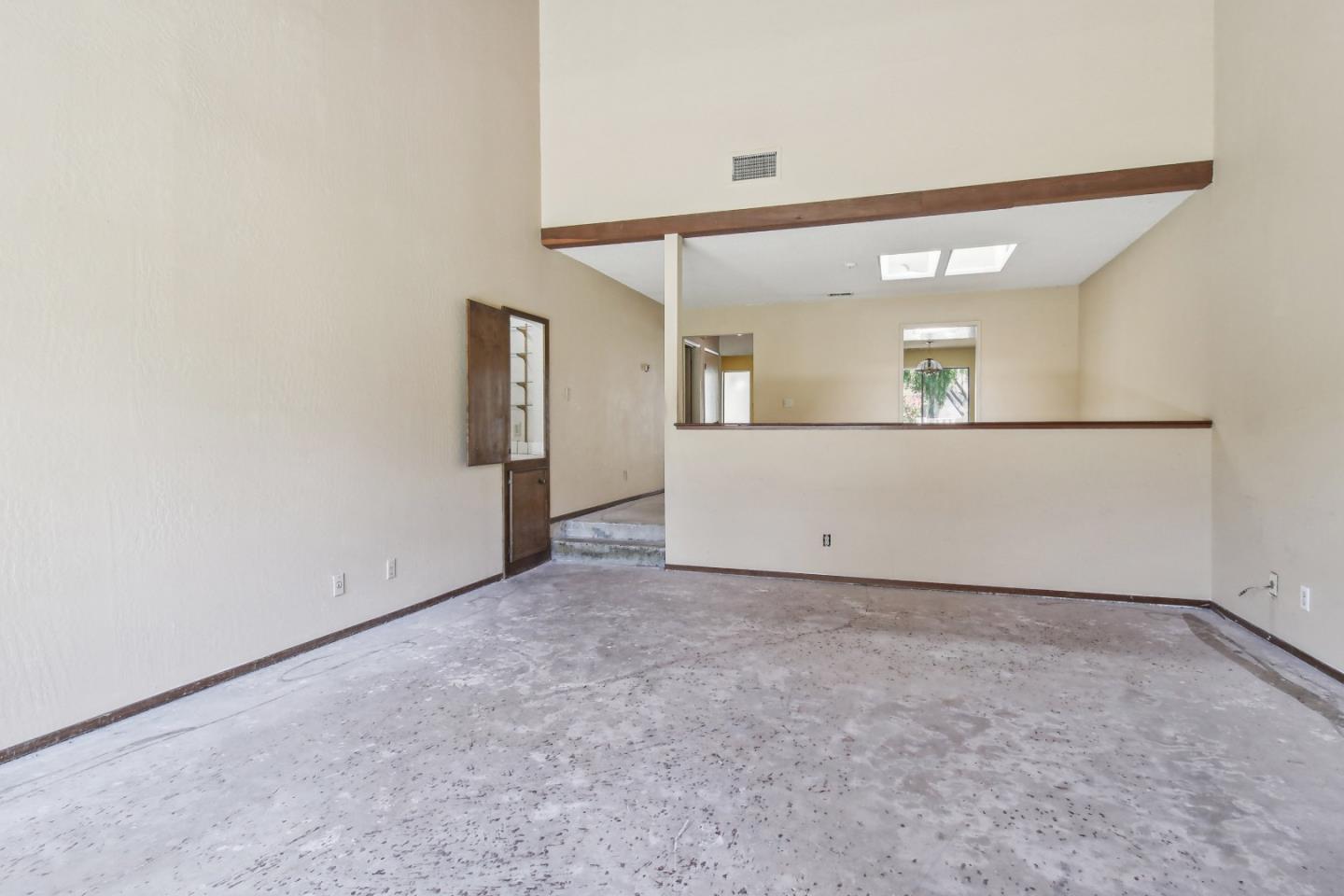 Empty living room with skylights, a half wall, and a worn bare floor.