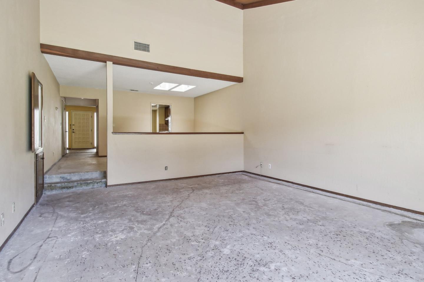 Vacant interior room with a cracked concrete floor and a half-height partition by the entry hall.