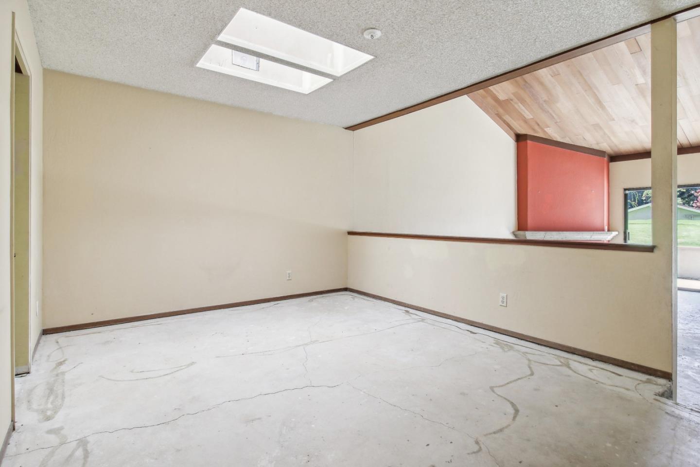 Vacant interior room with cracked concrete flooring, a pass-through ledge, and a sloped wood-paneled ceiling.
