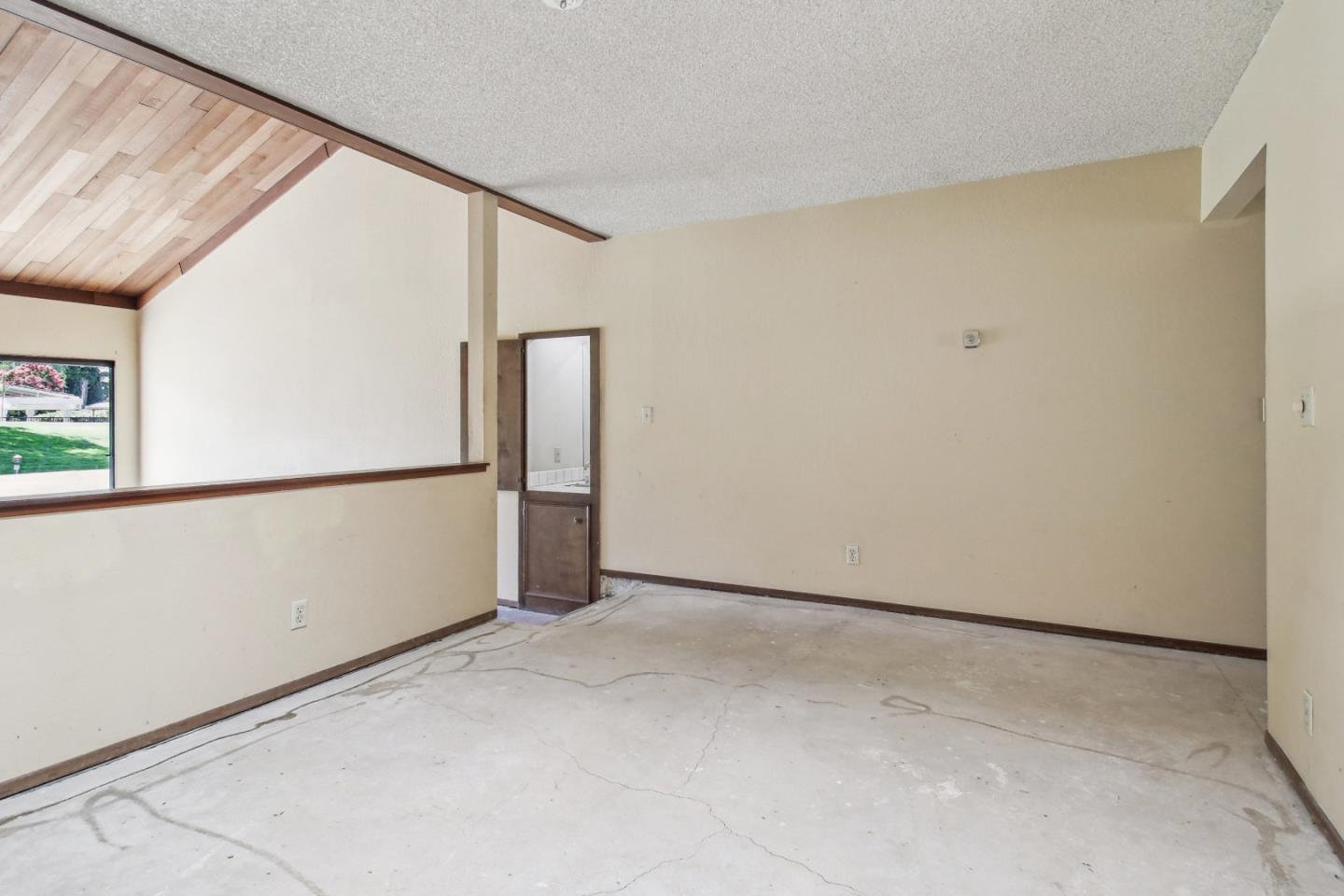 Empty room with a concrete floor, high wood-paneled ceiling, and window overlooking a lawn.