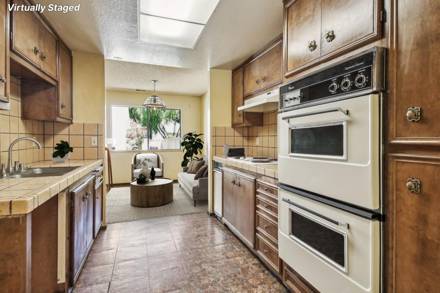 Kitchen with dark wood cabinets and double wall oven opening onto a staged sitting area.
