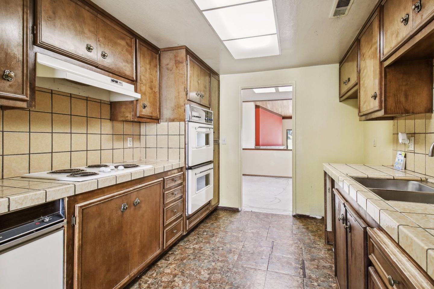 Kitchen with wood cabinets, tiled counters and backsplash, and built-in double ovens.