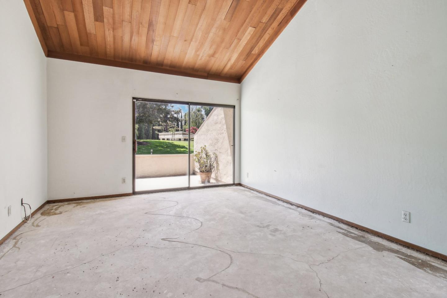 Empty living room with a vaulted wood ceiling and sliding doors to a patio and lawn.