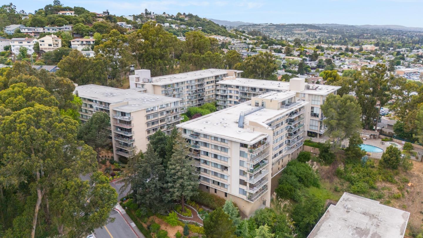 Aerial view of a condominium complex with a pool, wooded grounds, and hillside homes.