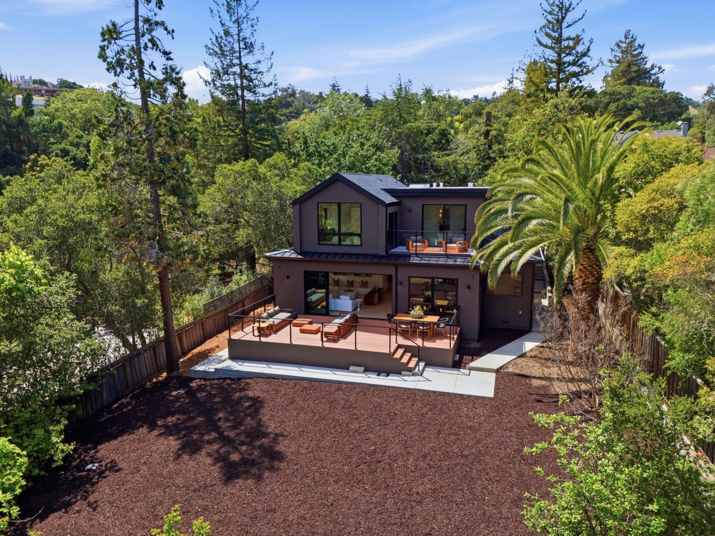 Aerial view of a modern home with expansive decks surrounded by mature trees and a palm.