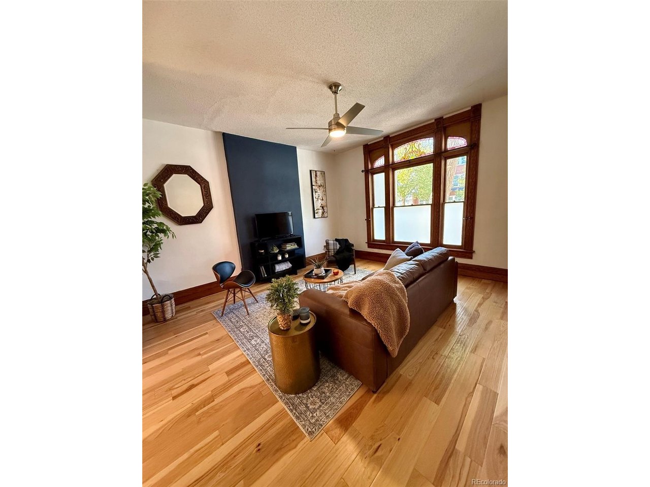 Furnished living room with stained-glass windows, hardwood floors, and a blue accent wall.