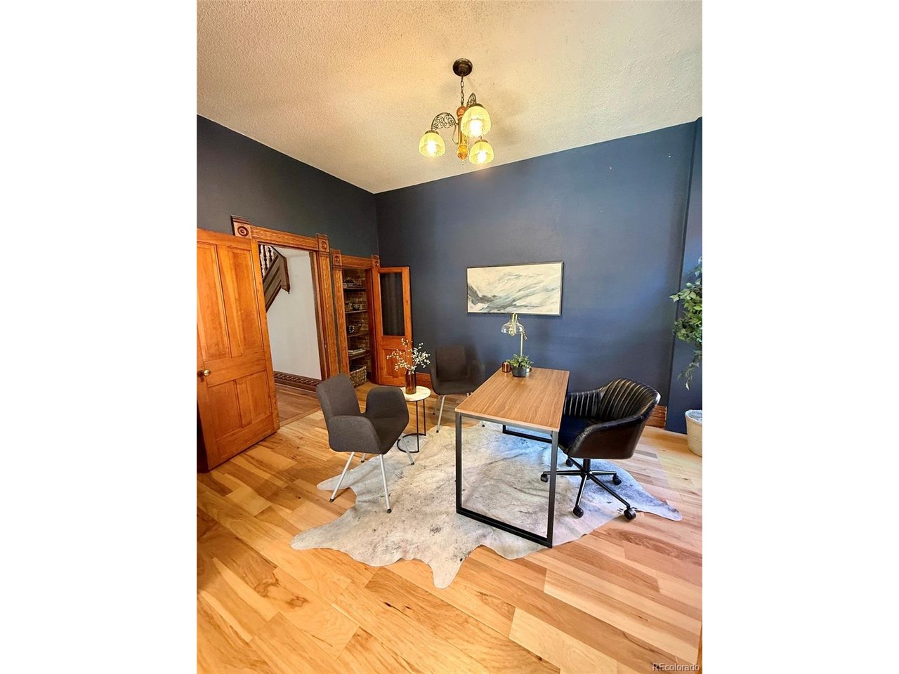 Office with deep blue walls, hardwood floors, ornate wood trim, and a desk with chairs.