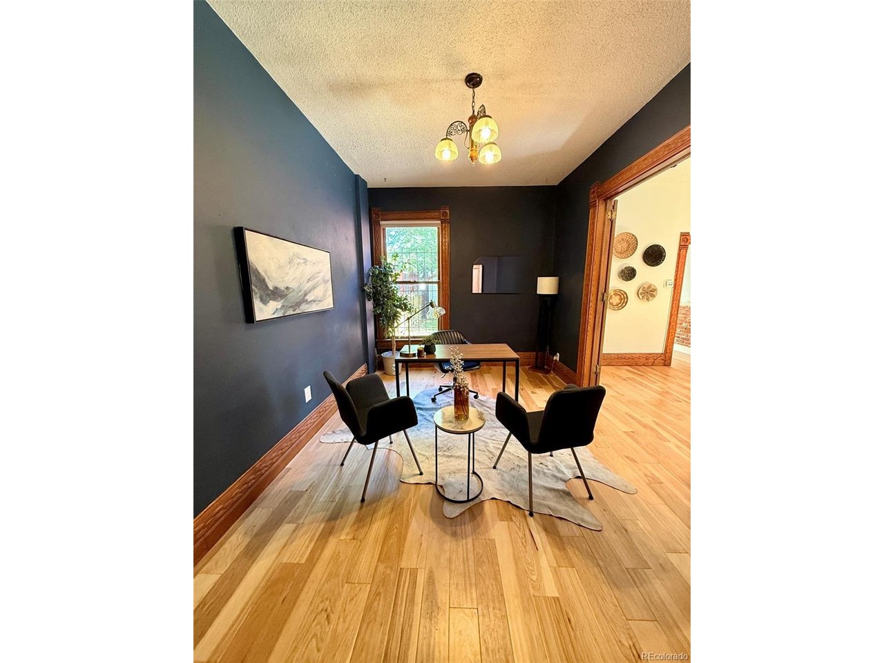 Furnished home office with dark walls, hardwood floors, and a desk facing two chairs.