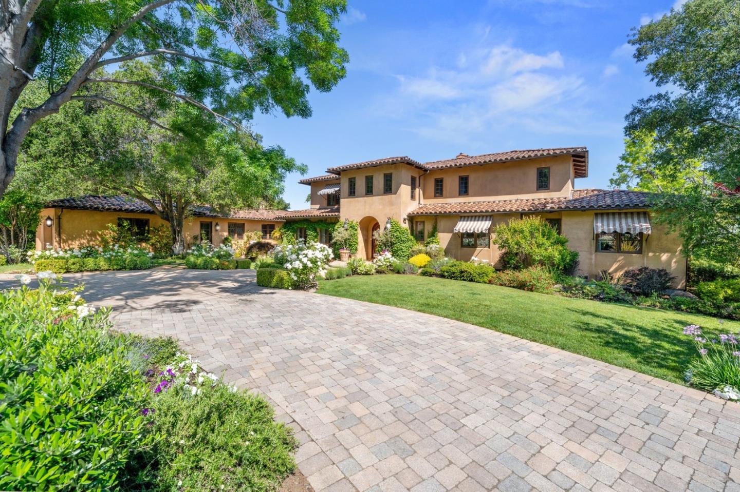Two-story stucco home with a tiled roof, landscaped garden, and broad paved driveway.